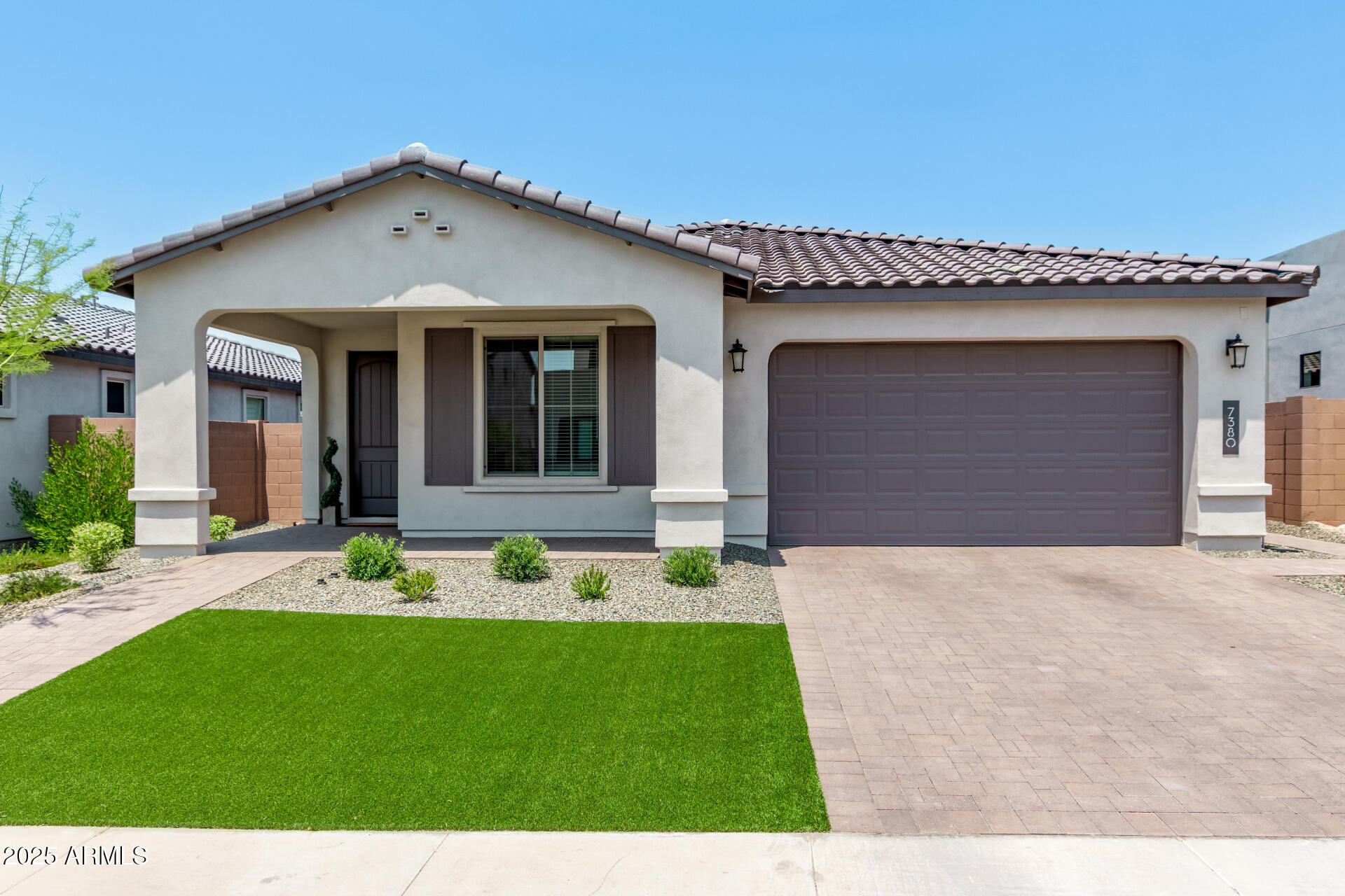 Single-story stucco home with a tiled roof, covered entry, two-car garage, and artificial-turf lawn.