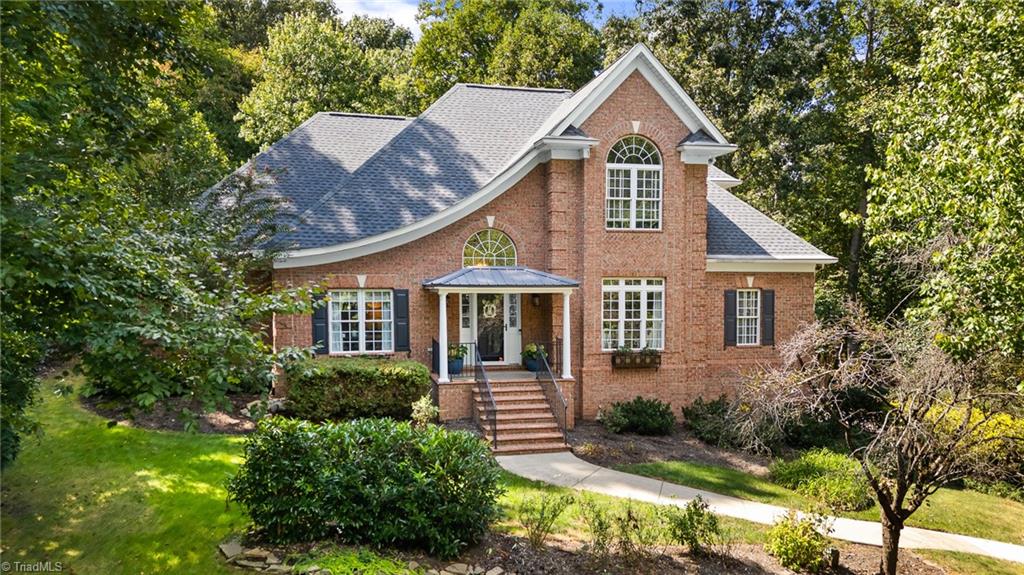 Two-story red brick house with an arched upper window, covered entry, and mature trees.