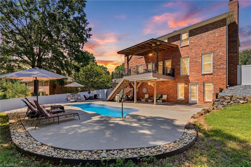 Brick home with an elevated covered deck overlooking a backyard pool and patio at sunset.