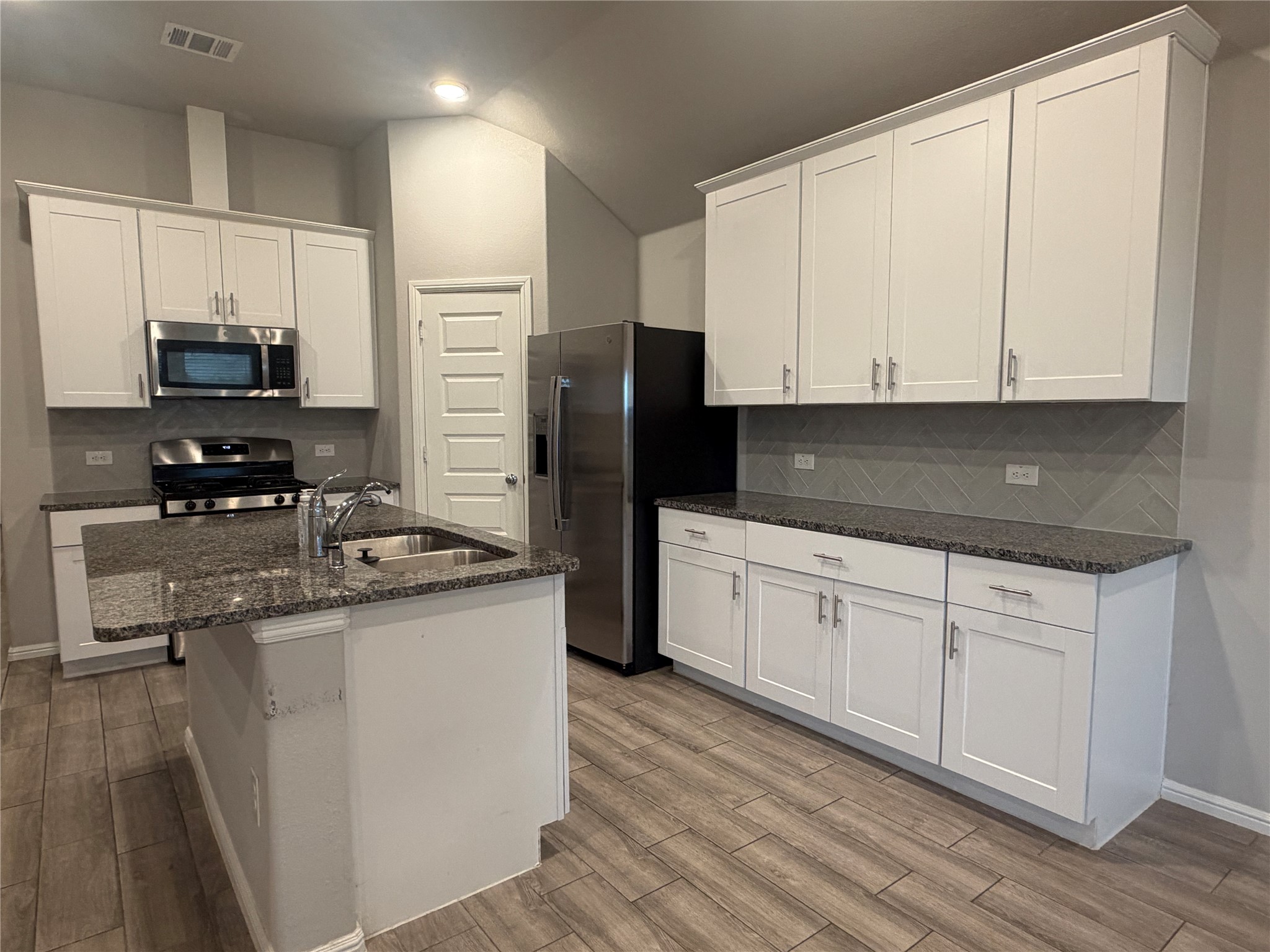 Kitchen with white cabinets, granite counters, a sink island, and stainless steel appliances.