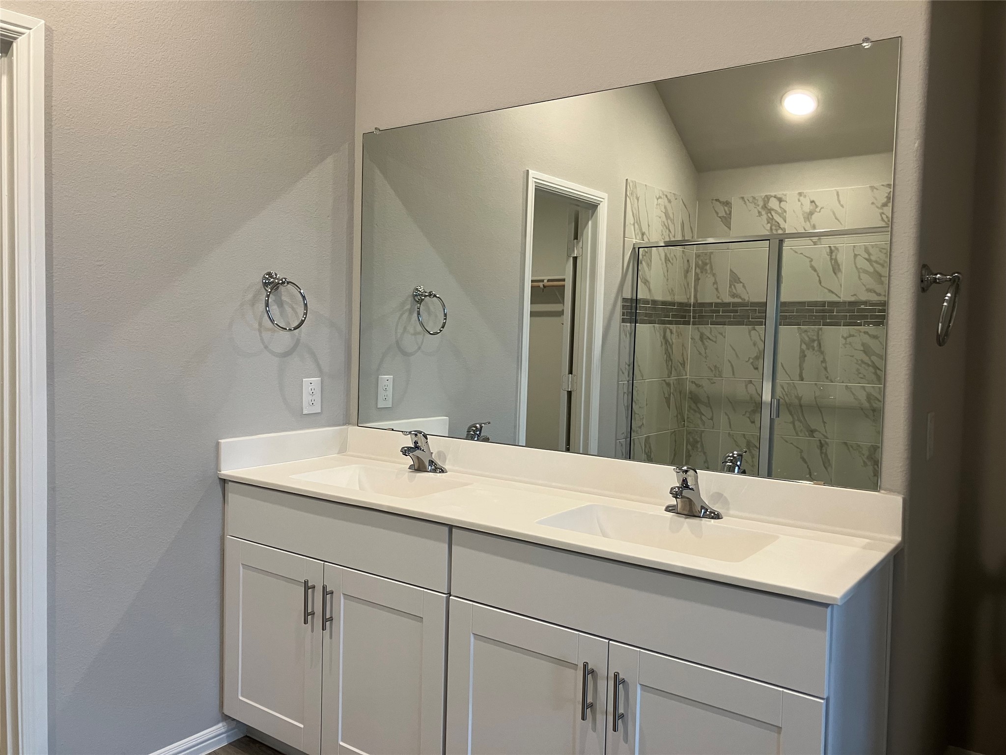 Bathroom with a double-sink vanity and mirrored wall facing a glass shower with marble-look tile.