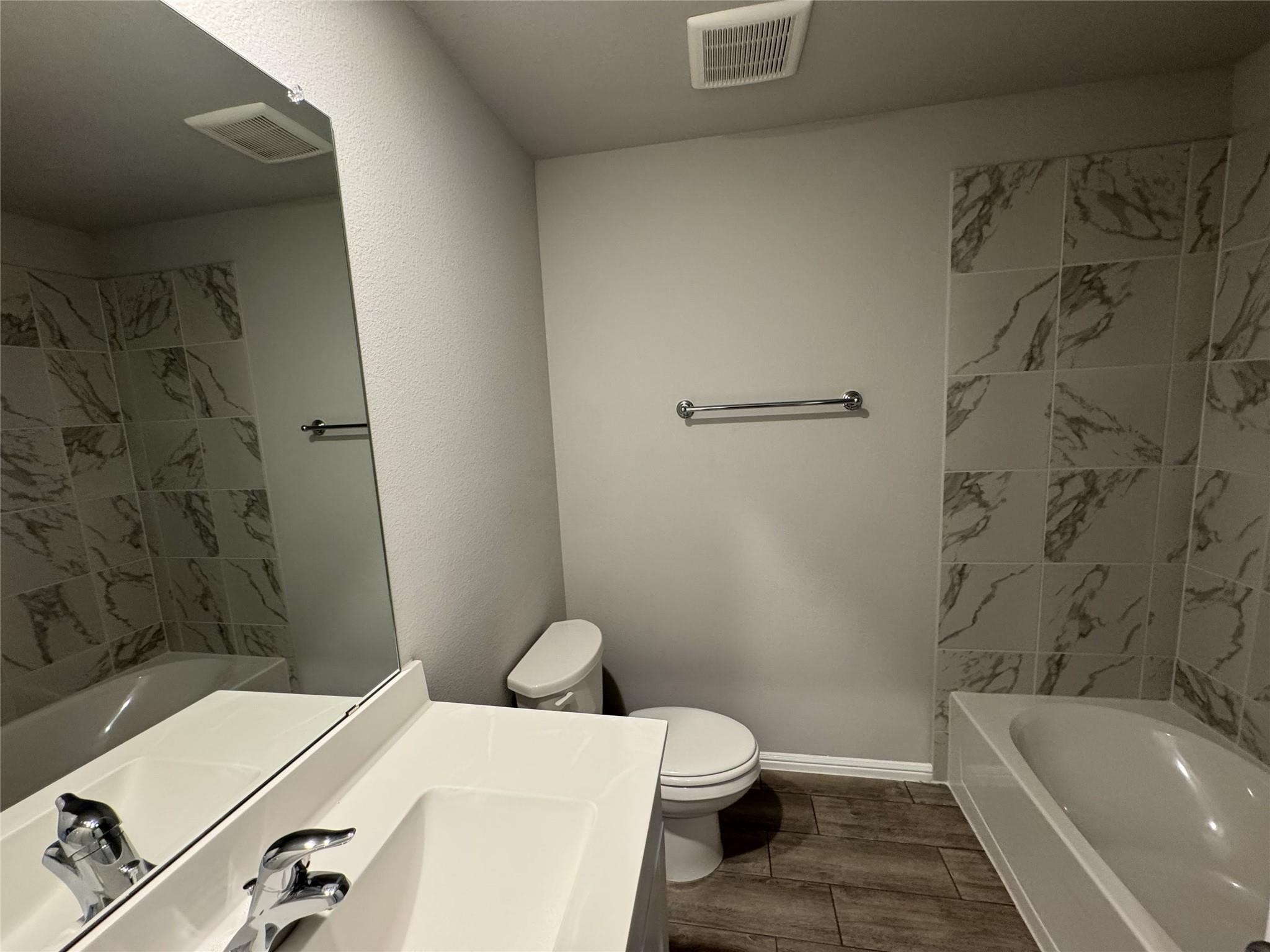 Bathroom with a white vanity, toilet, and bathtub surrounded by gray marble-look tile.
