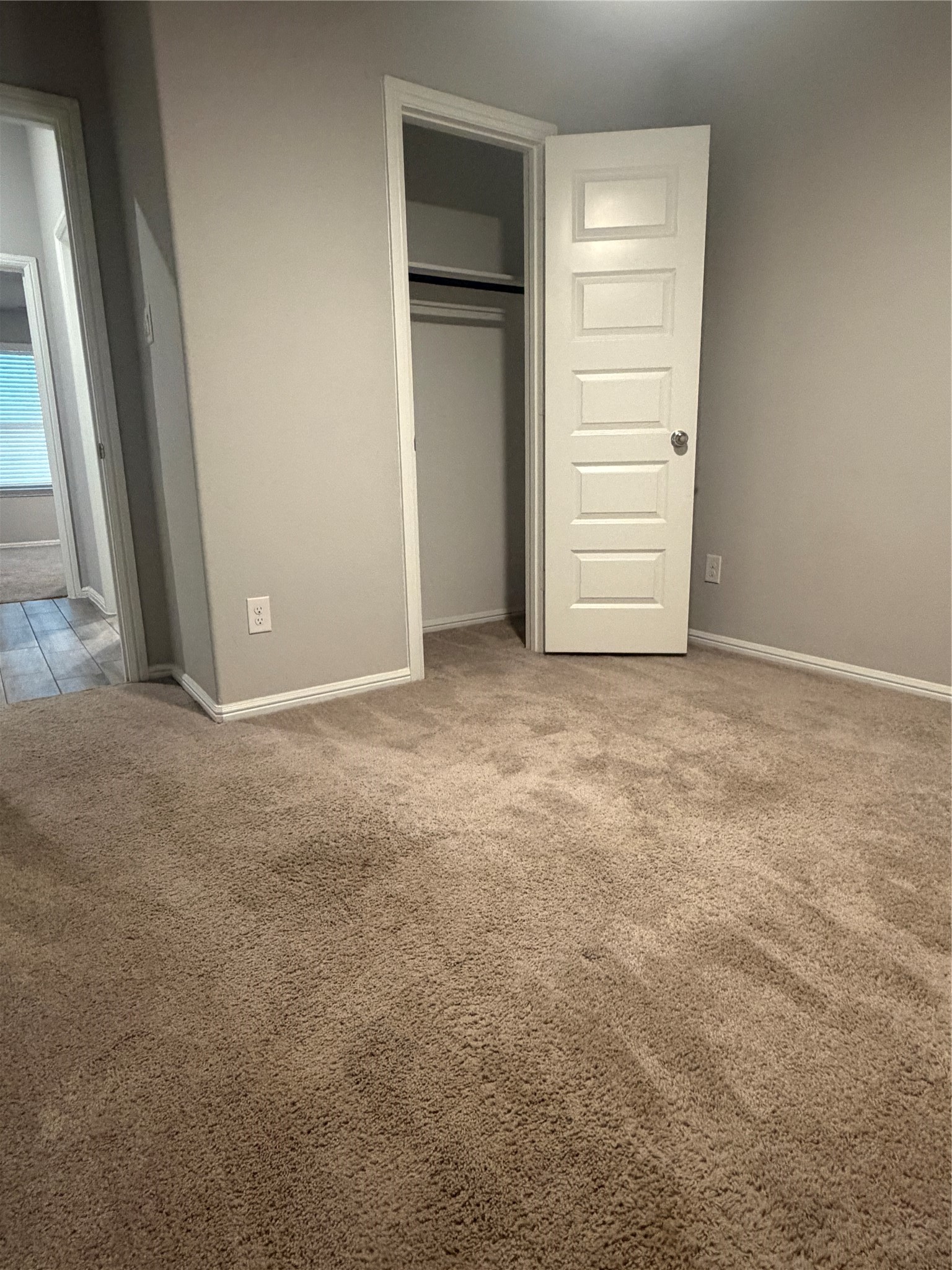 Empty bedroom with beige carpet and an open closet door.