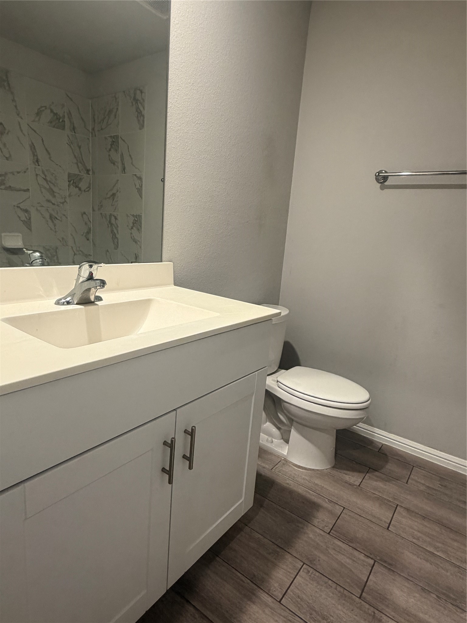 Bathroom with a white vanity, toilet, marble-look wall tiles, and dark wood-look flooring.