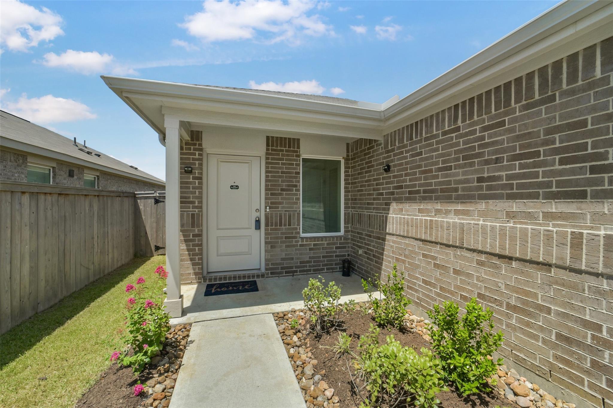 Covered brick front entry with a white door, walkway, and landscaped flower beds.