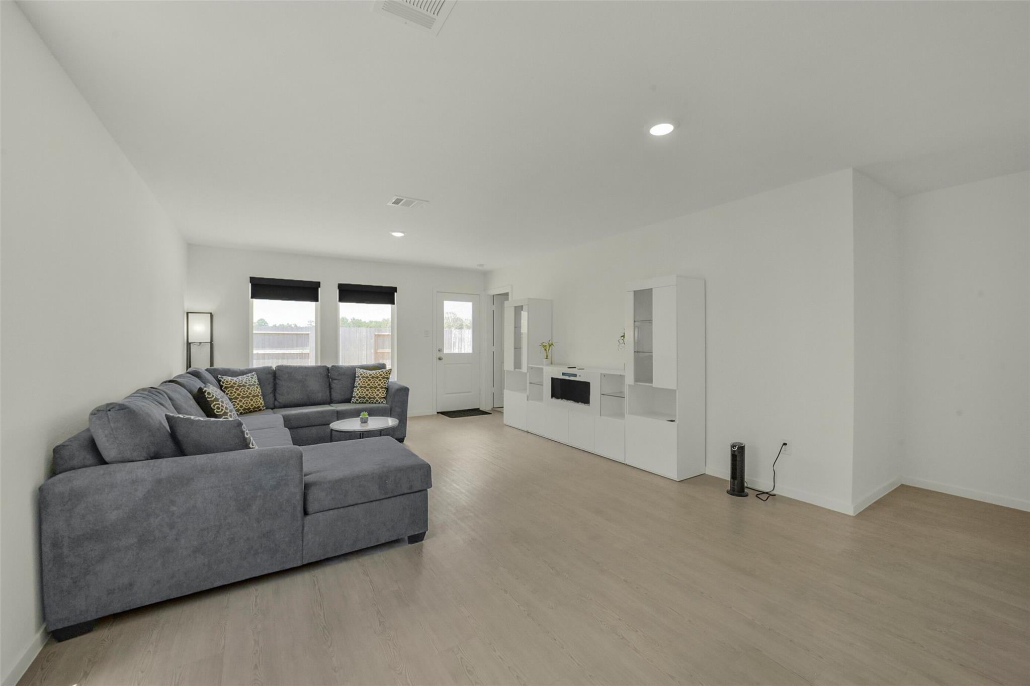 Living room with a gray sectional sofa, light wood floors, and white entertainment cabinetry.
