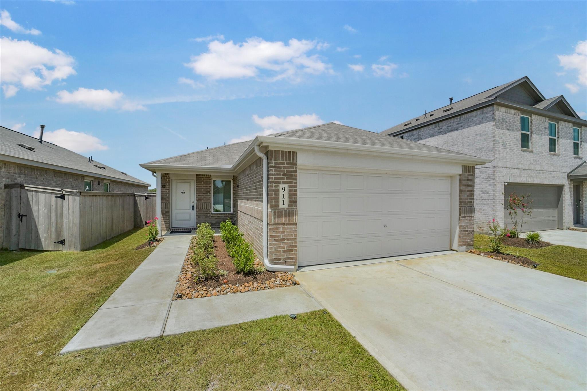 Brick single-story home with a wide white garage, concrete driveway, and fenced side yard.