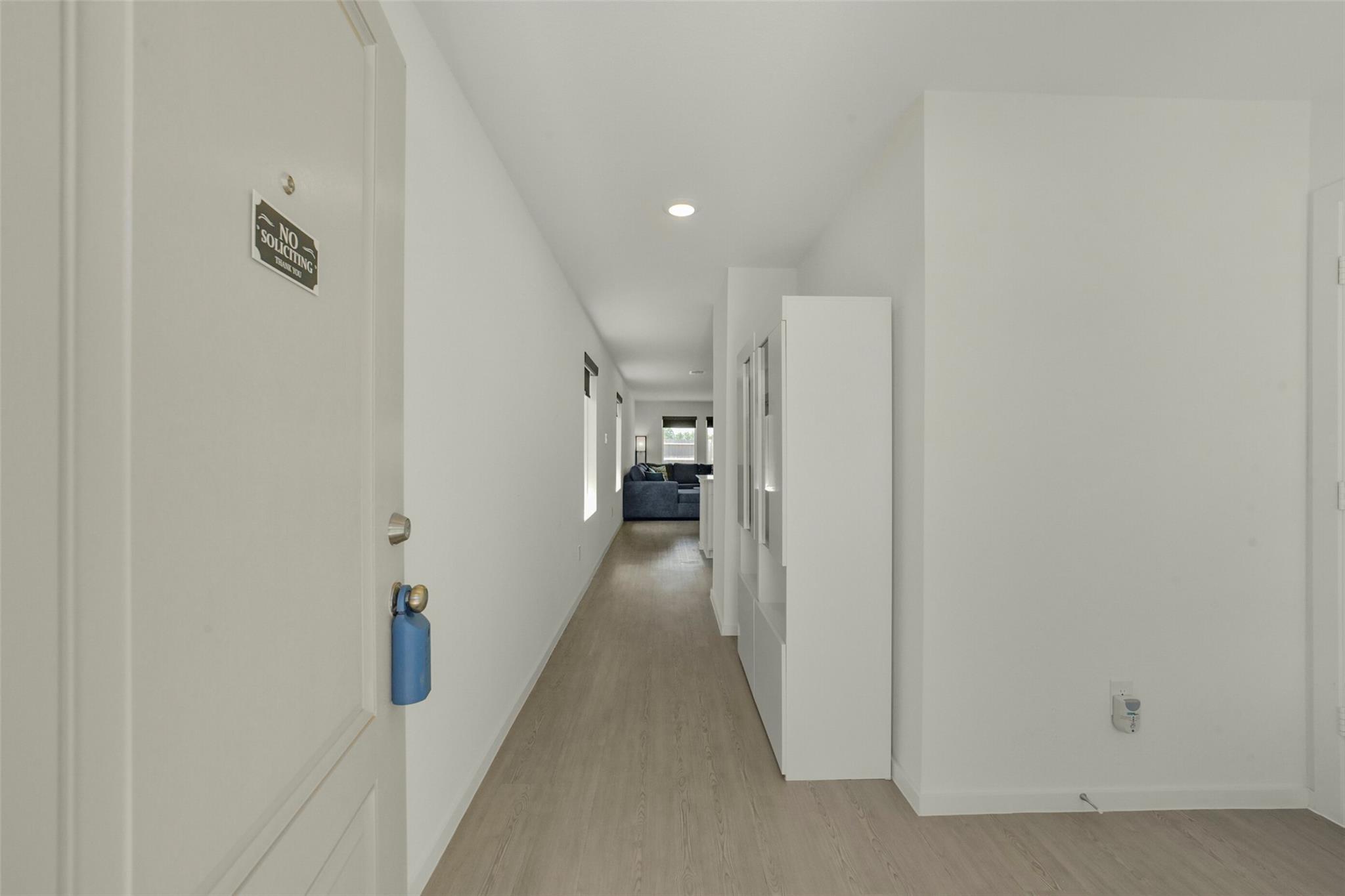 Bright entry hallway with light wood flooring, white built-in cabinetry, and a dark sofa at the far end.