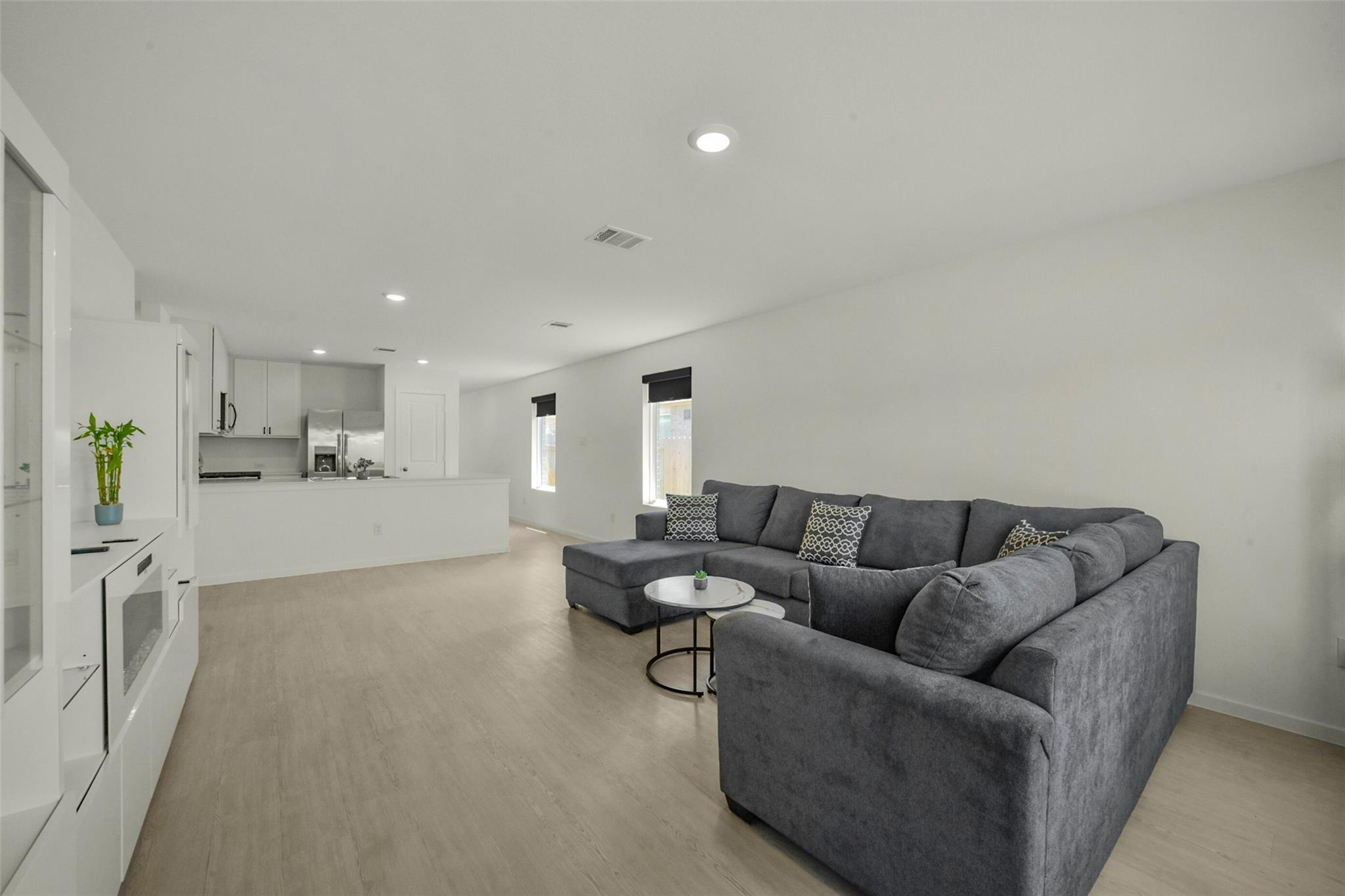 Open-plan living room with a large gray sectional and white kitchen cabinetry.