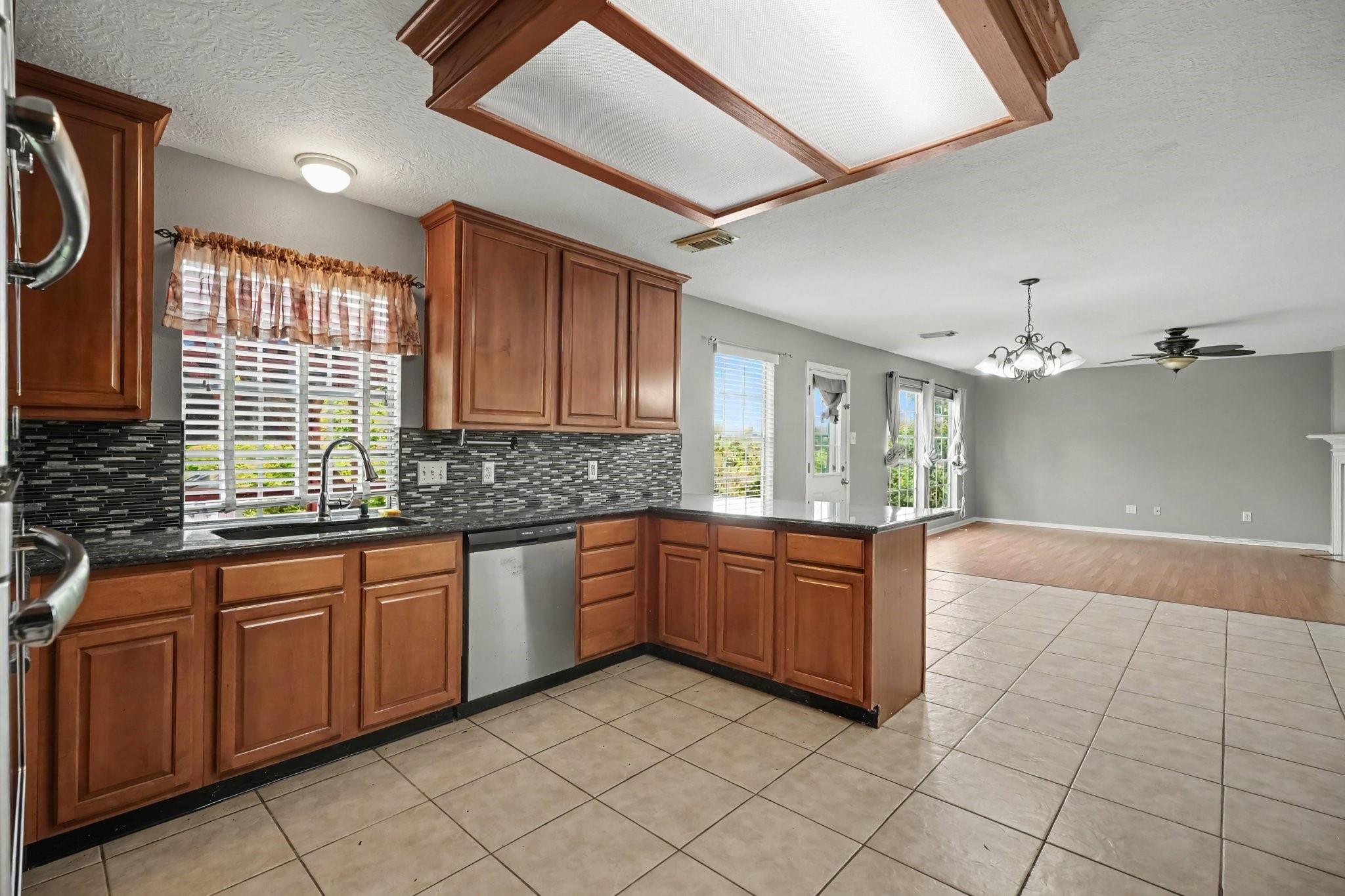 Kitchen with wood cabinets and mosaic backsplash opening to a living area