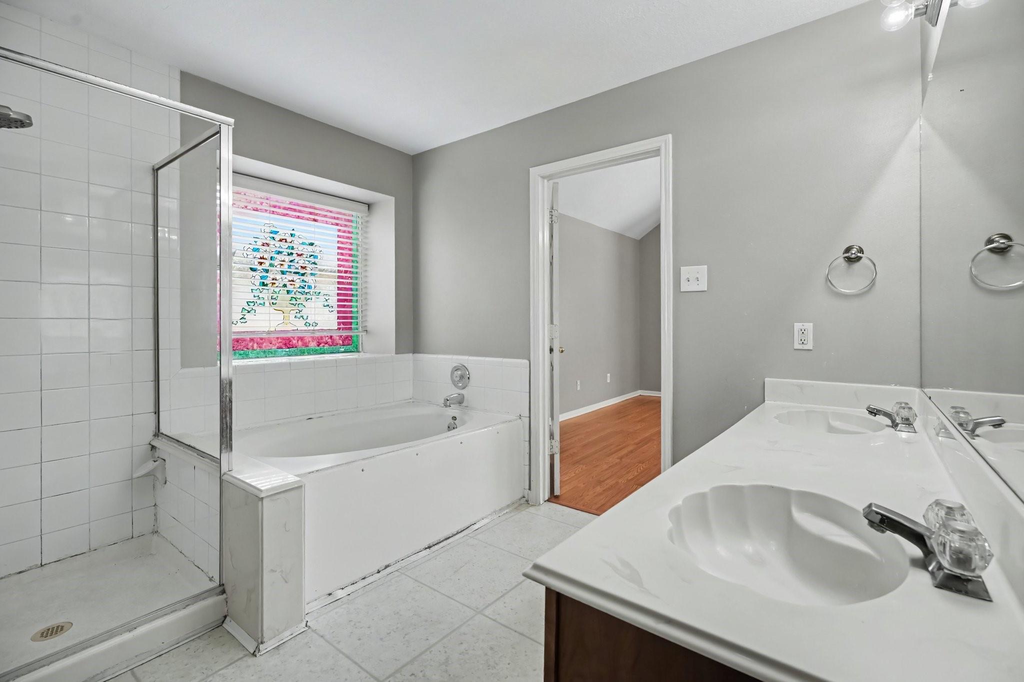 Bathroom with a glass shower, bathtub beneath a colorful window blind, and double-sink vanity.