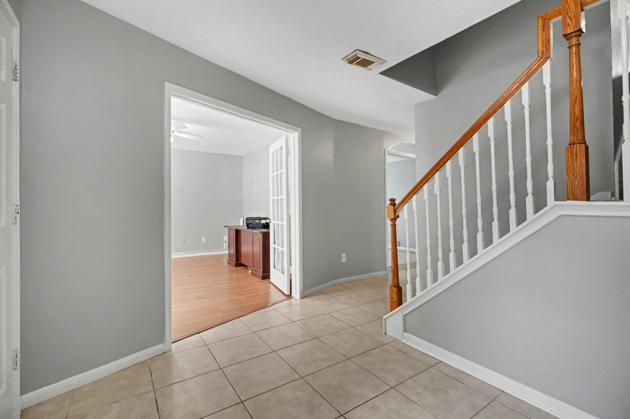 Entry hall with tiled floor and a staircase featuring white balusters and a wood handrail.