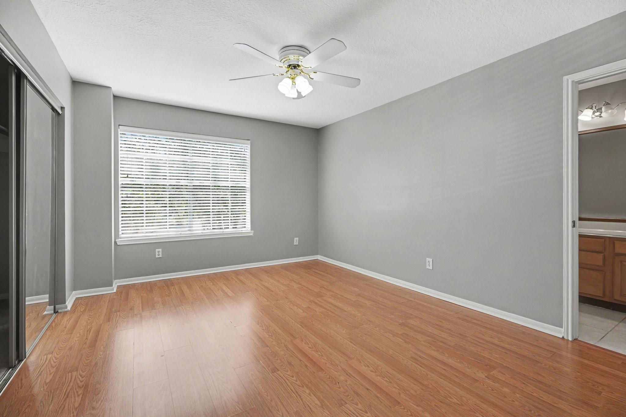 Empty bedroom with mirrored closet doors, wood flooring, and a ceiling fan.