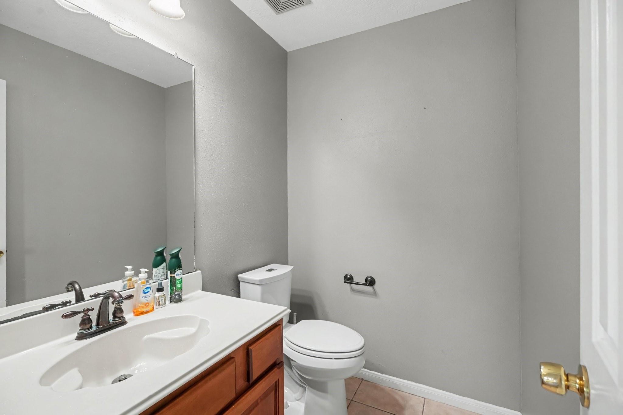 Bathroom with a large mirror, white countertop, wooden vanity, and toilet.
