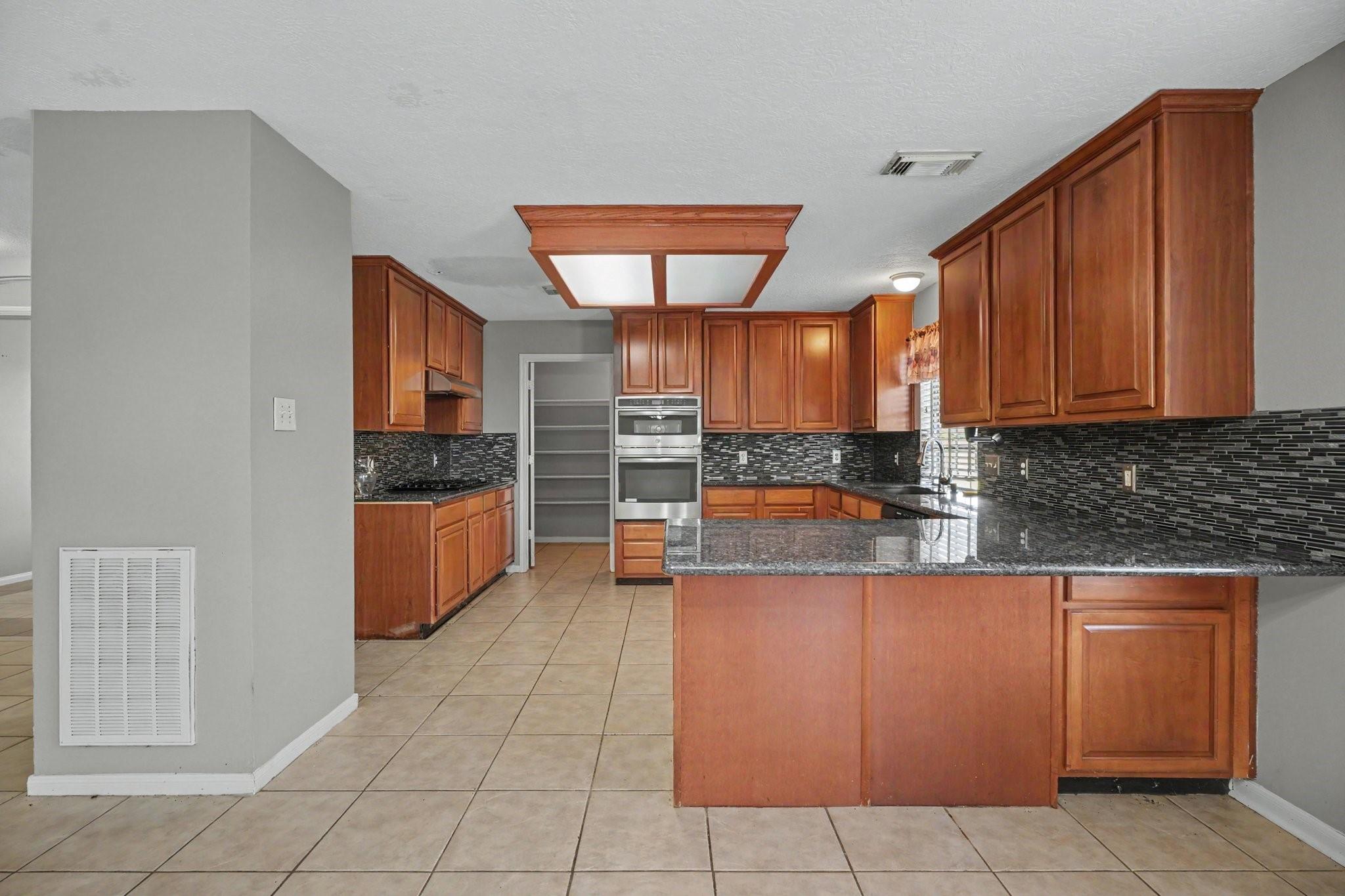 Kitchen with wood cabinets, granite island, mosaic backsplash, and stainless steel double ovens.
