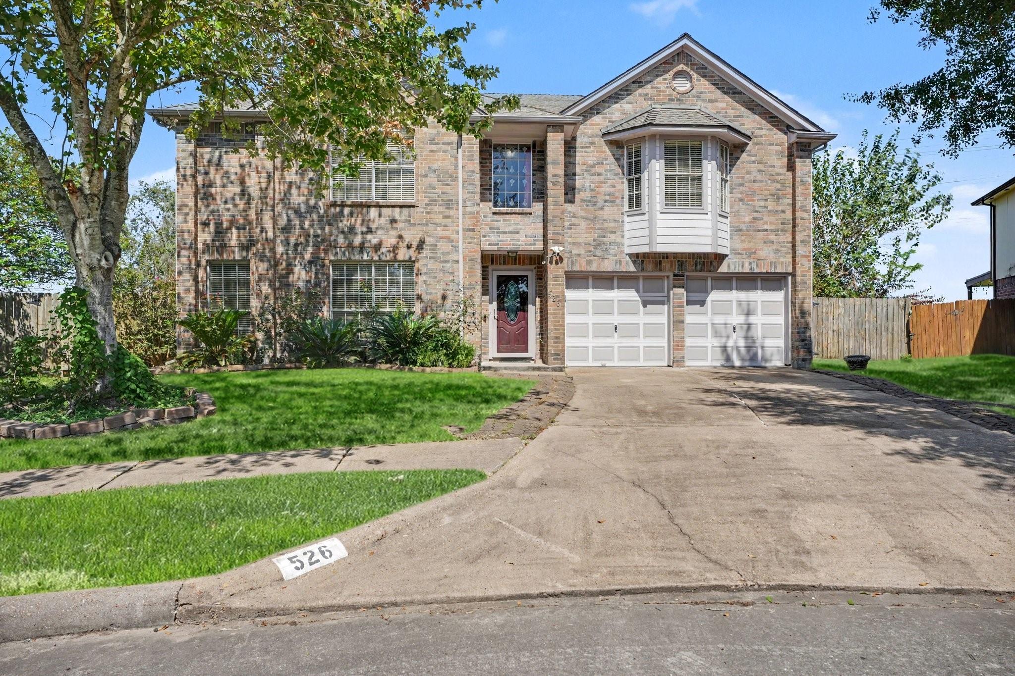 Two-story brick house with a bay window, red front door, and wide driveway.