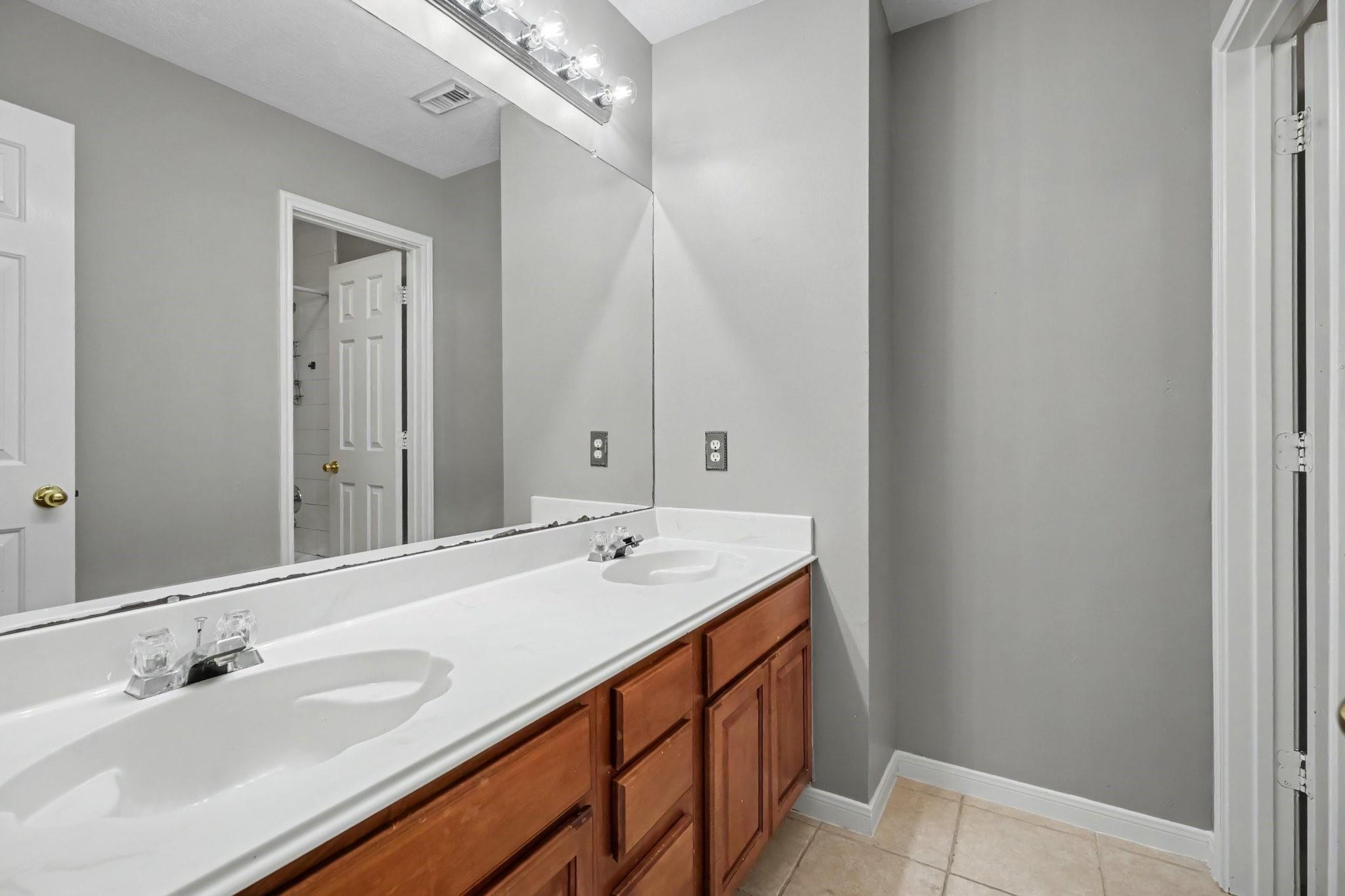 Bathroom with a double-sink vanity, wood cabinets, and a large mirror.
