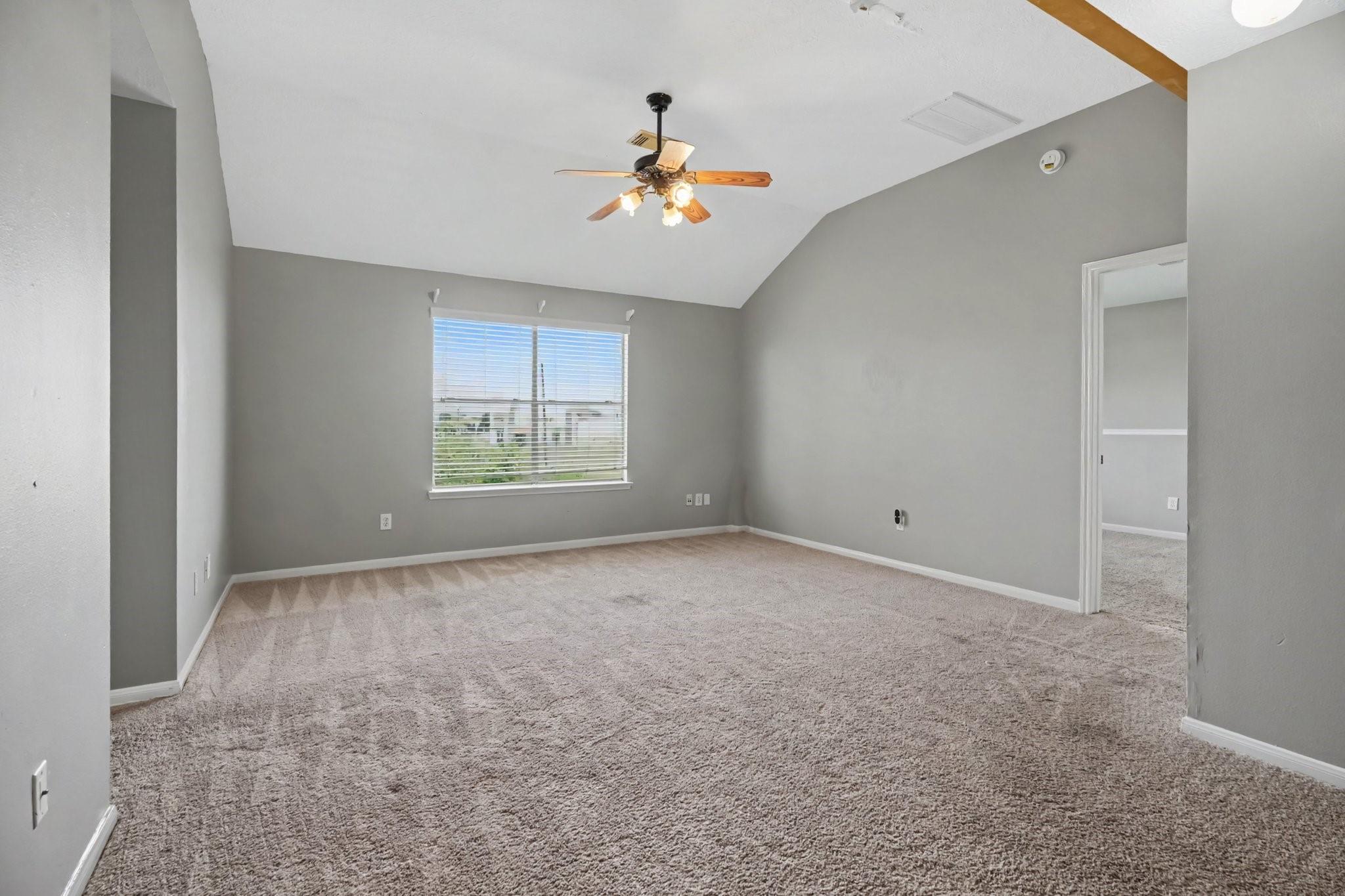 Empty carpeted bedroom with gray walls, a vaulted ceiling, and a window with blinds.