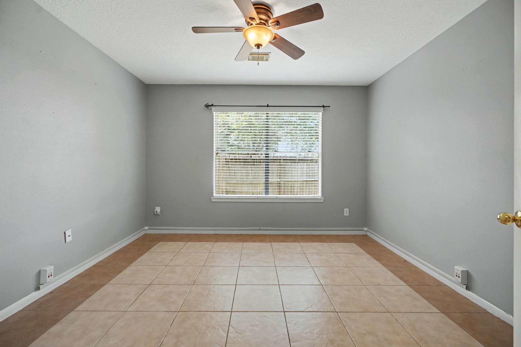 Empty gray room with beige tile flooring, a ceiling fan, and a window with blinds.