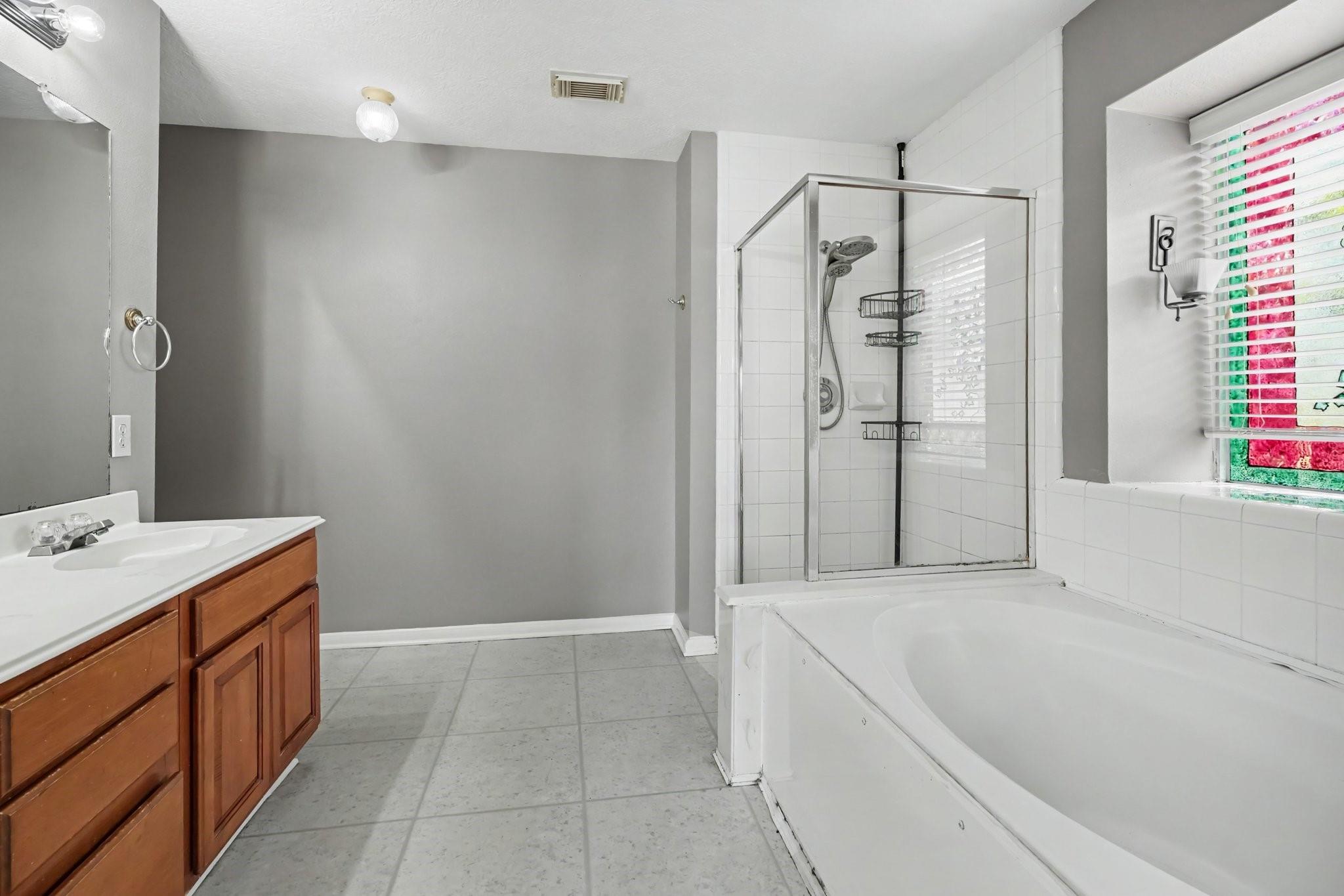Bathroom with a large soaking tub, glass-enclosed shower, and wood vanity.