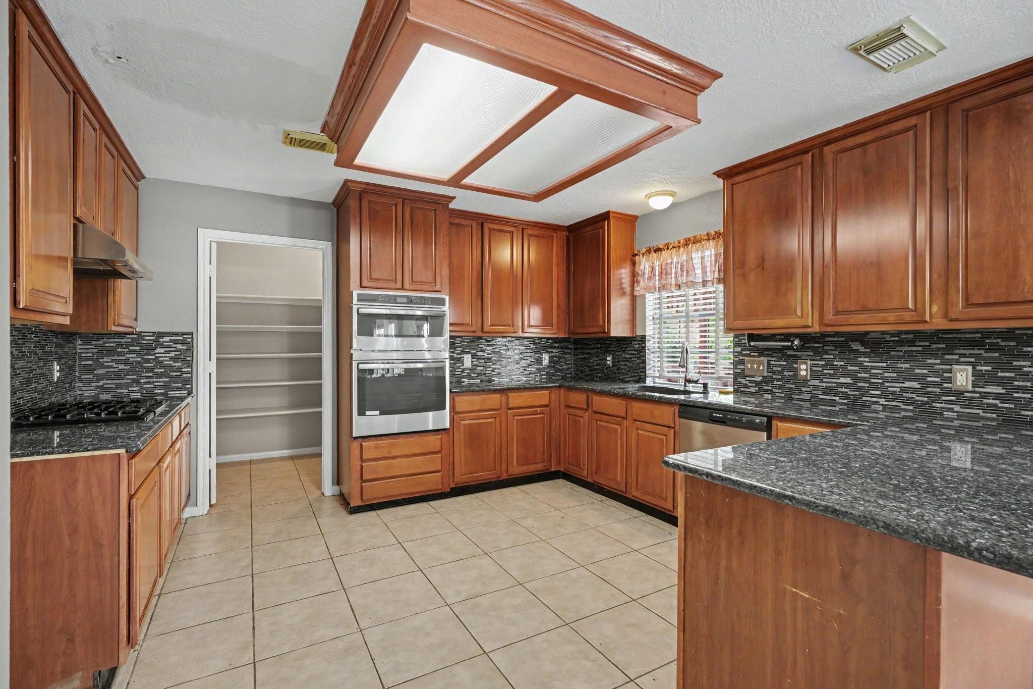 Kitchen with warm wood cabinetry, dark granite counters, mosaic backsplash, and stainless steel double ovens.