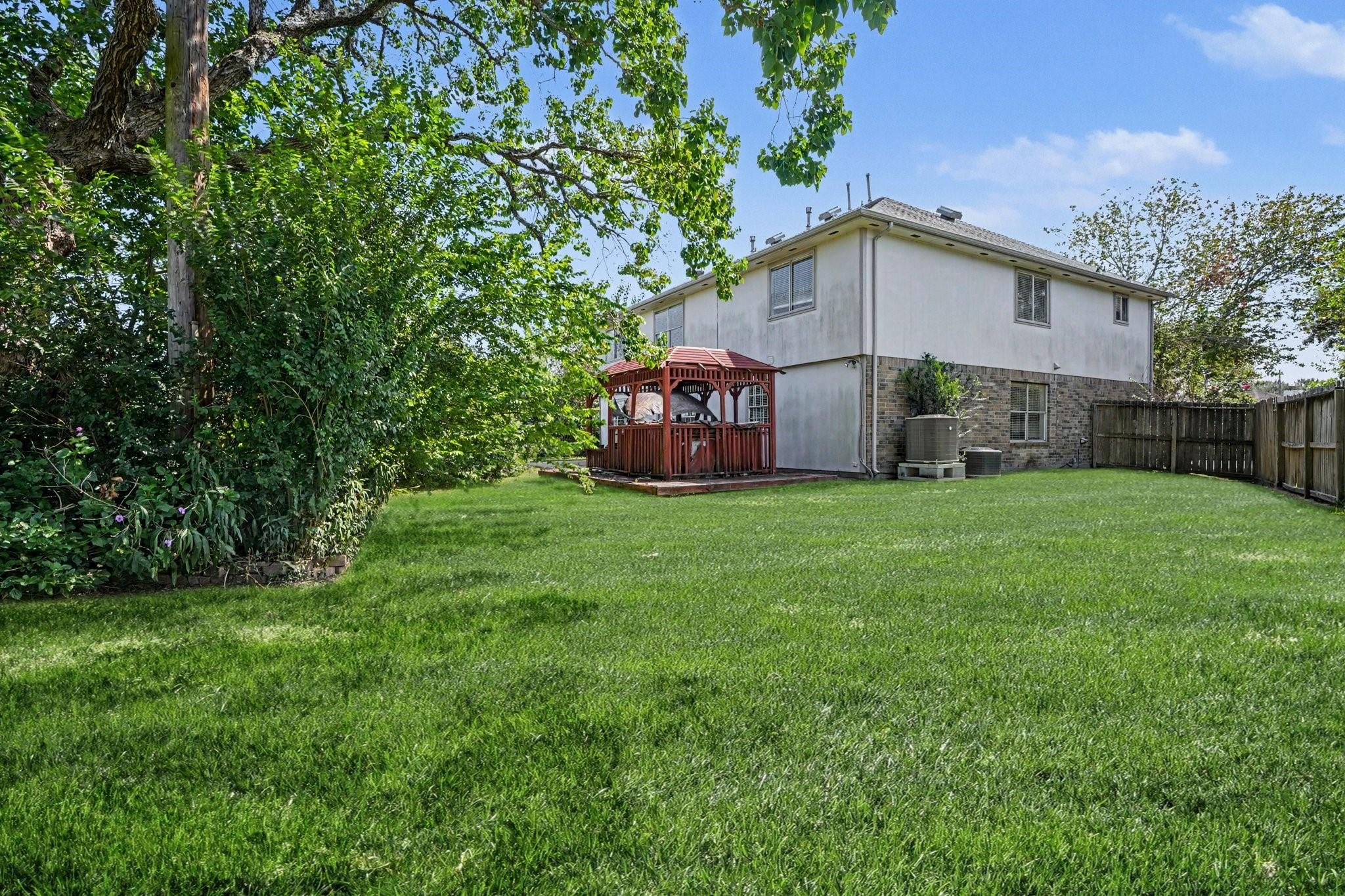 Two-story home with a red gazebo beside a spacious lawn and fenced backyard.