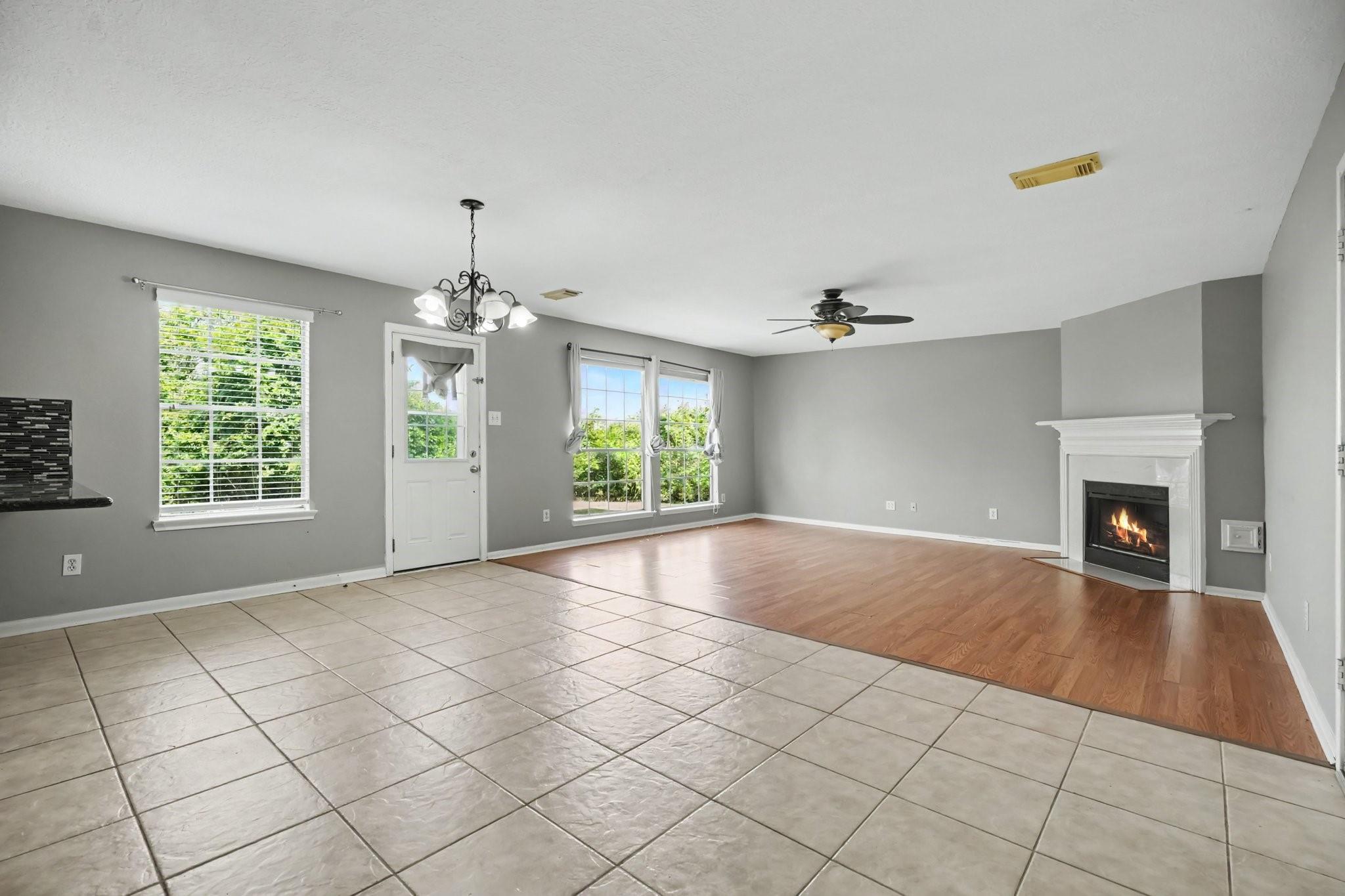 Vacant living room with a white fireplace, gray walls, and tile flooring transitioning to wood.