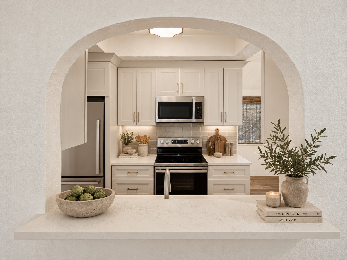 Kitchen framed by a white arch, with cream cabinets, stainless appliances, and a marble island.