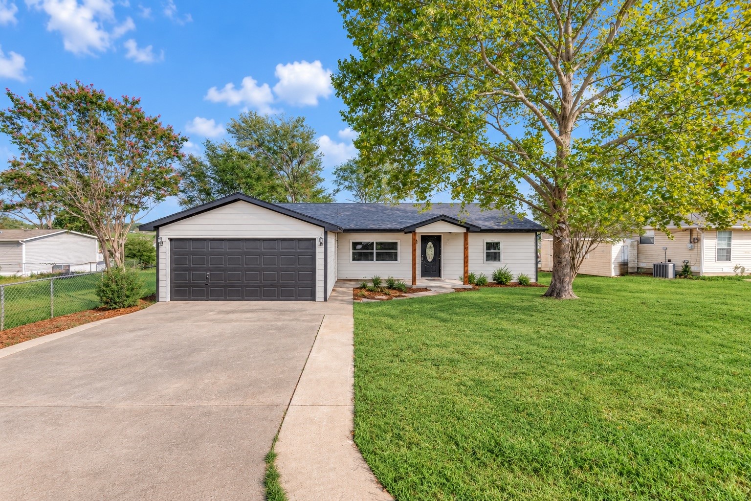 Single-story house with a wide dark garage, concrete driveway, and mature trees.
