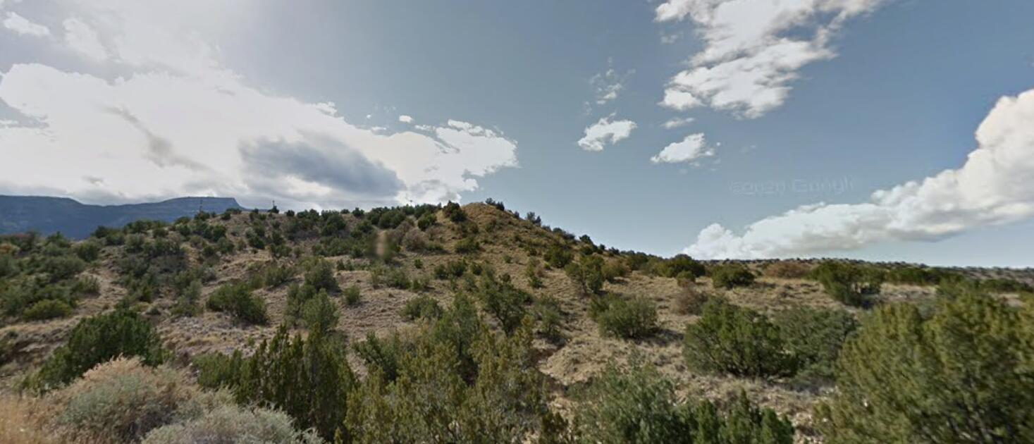 Placitas foothills covered in low shrubs, with a distant mountain ridge beneath a partly cloudy sky.