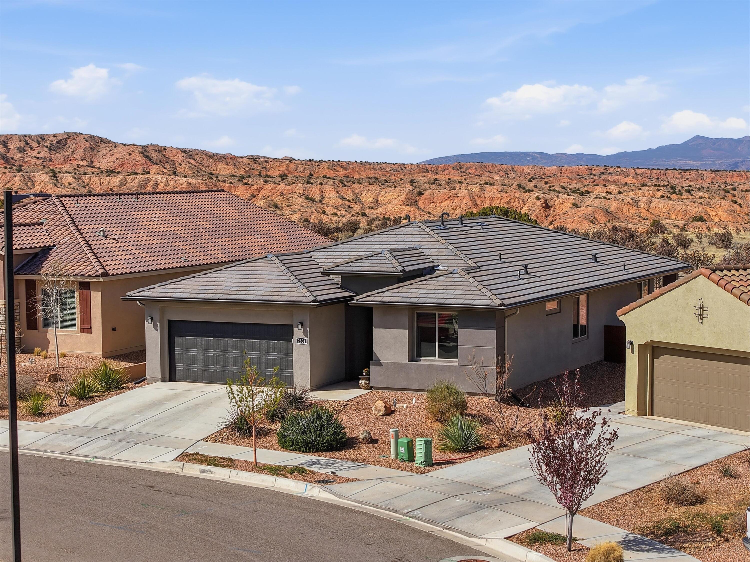 Single-story stucco home with a dark tile roof, desert landscaping, and rocky mountain views.