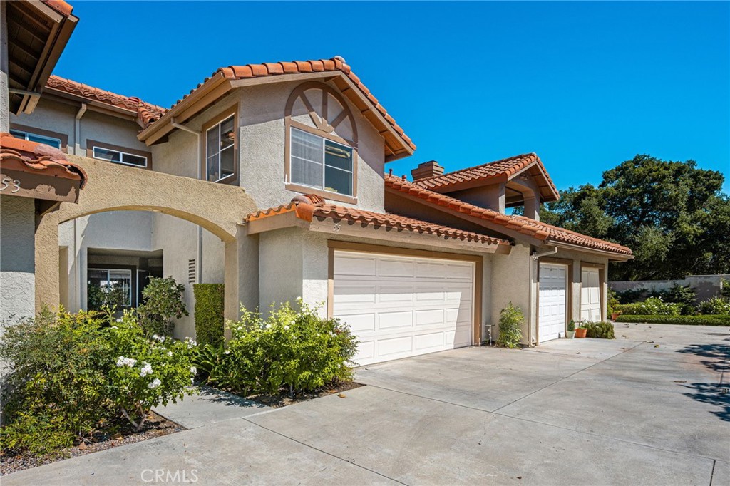 Two-story stucco home with terracotta tile roofs, arched entry, white garage doors, and a broad driveway.