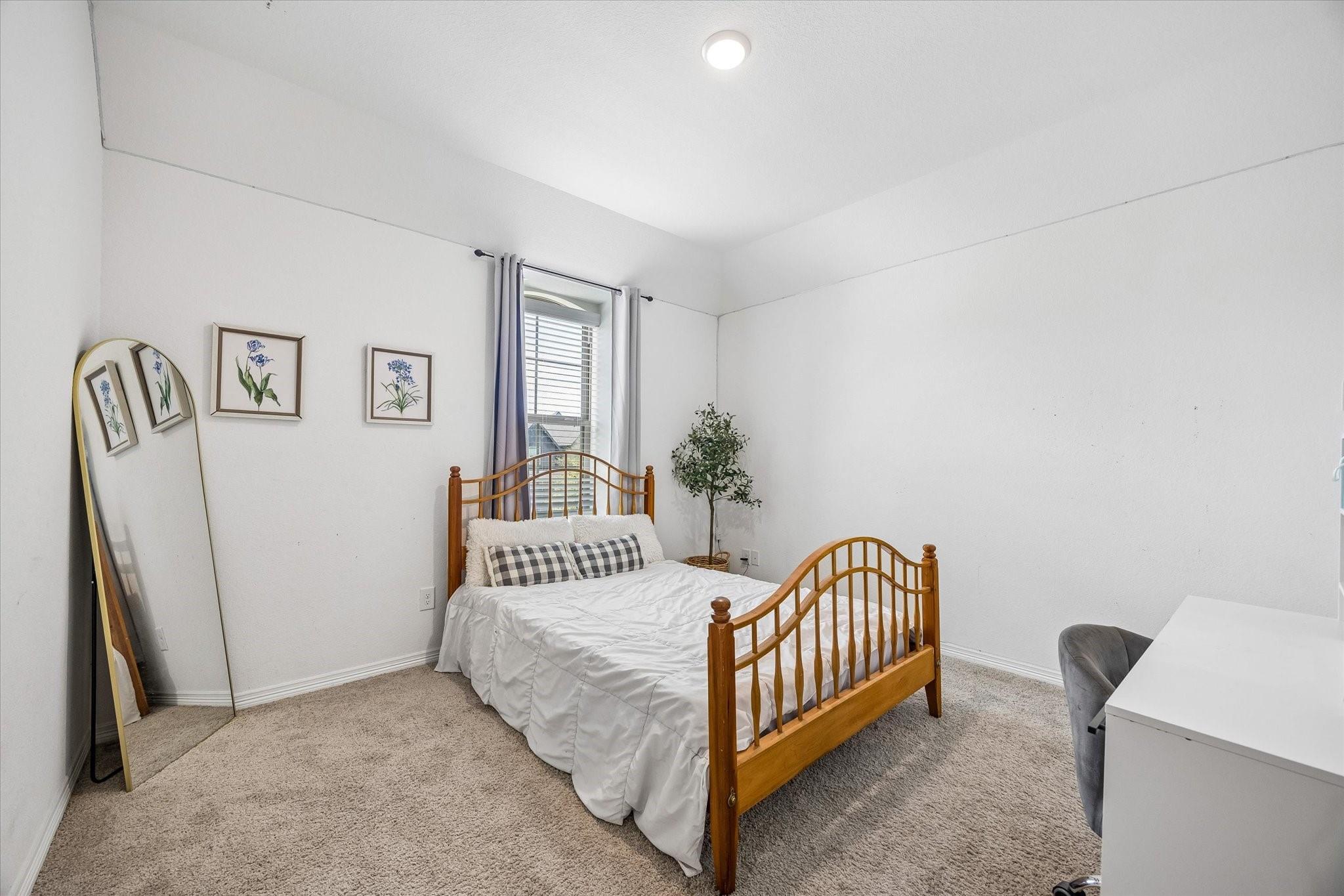 Furnished bedroom with a wooden bed, checkered pillows, botanical prints, and a full-length mirror.