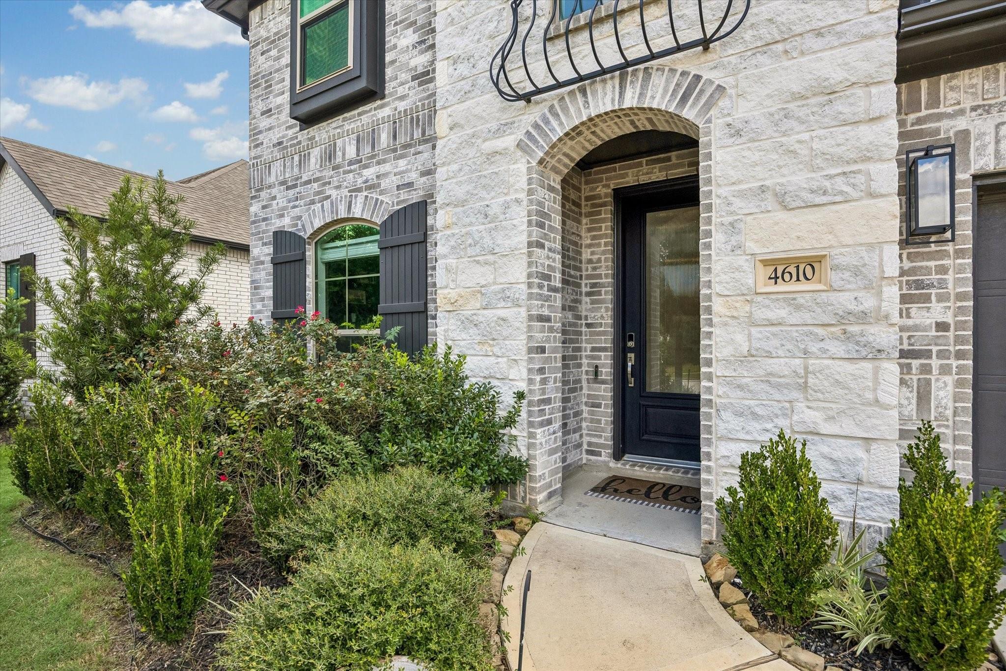 Arched stone entry with a black front door, address plaque, and landscaped shrubs.