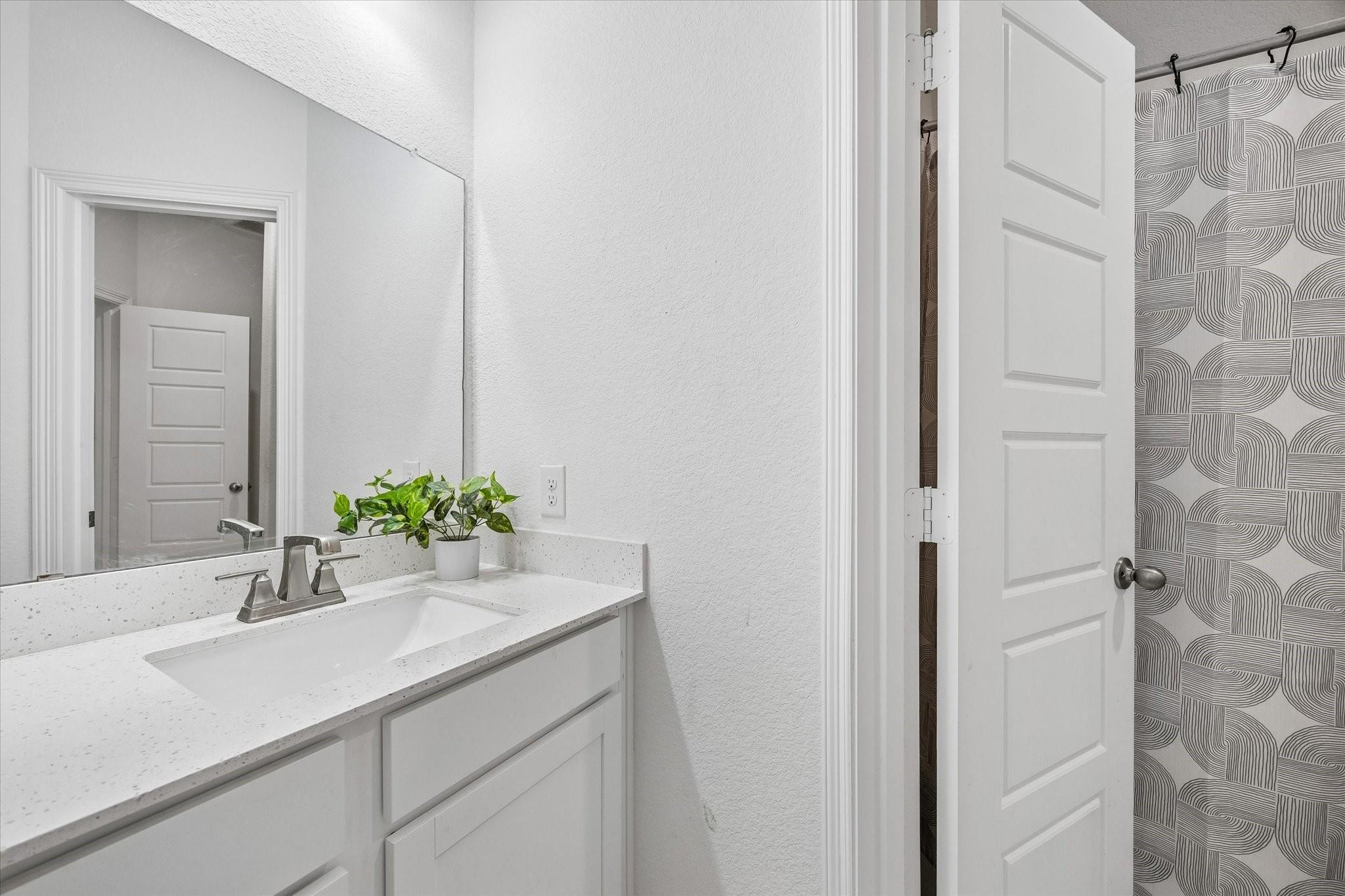 Bathroom vanity with a speckled countertop, large mirror, and patterned shower curtain.