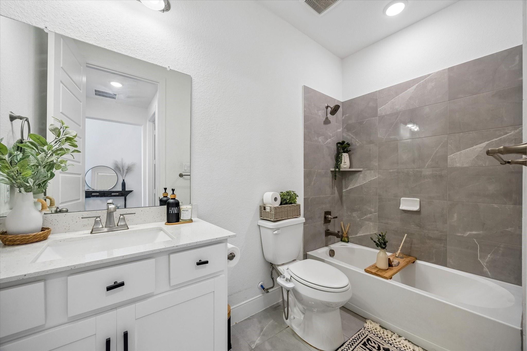 Bathroom with a white vanity, toilet, and bathtub featuring a gray tile surround.