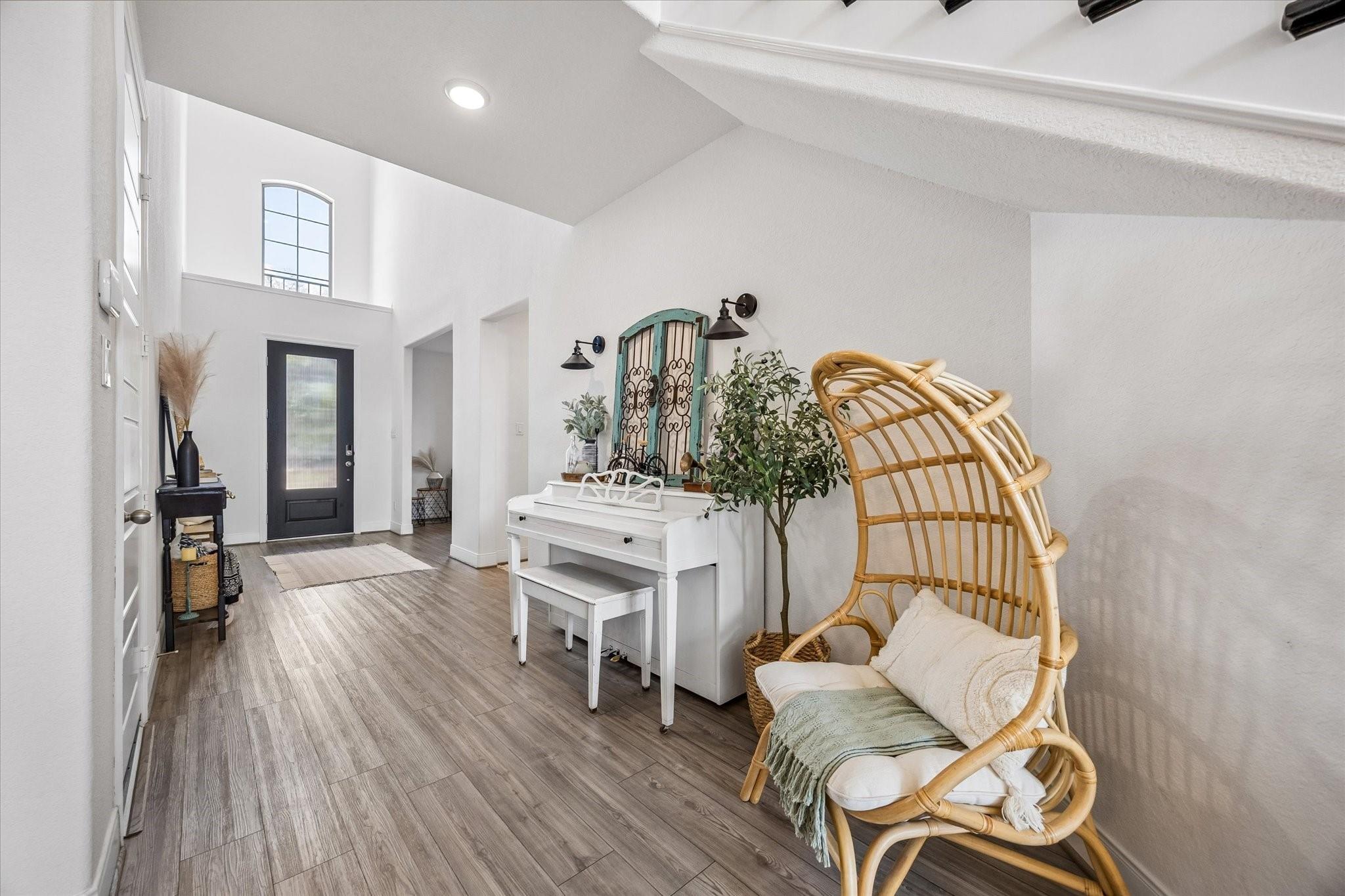 Two-story entry foyer with a black front door, white piano, and wicker hanging chair.