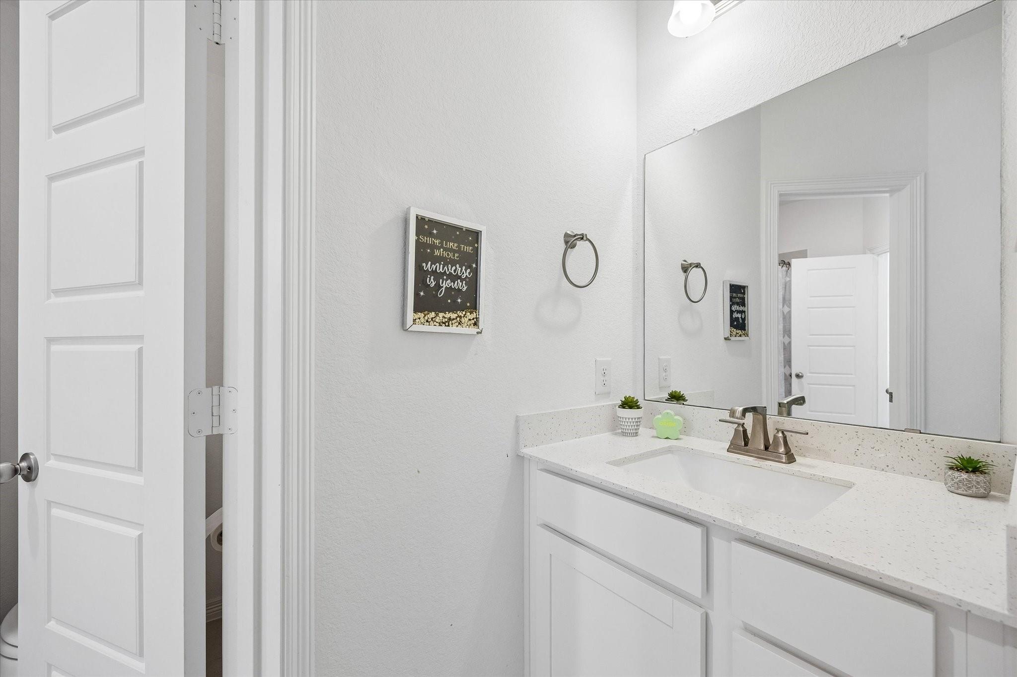 Bathroom vanity with a large mirror, speckled countertop, and framed inspirational sign.