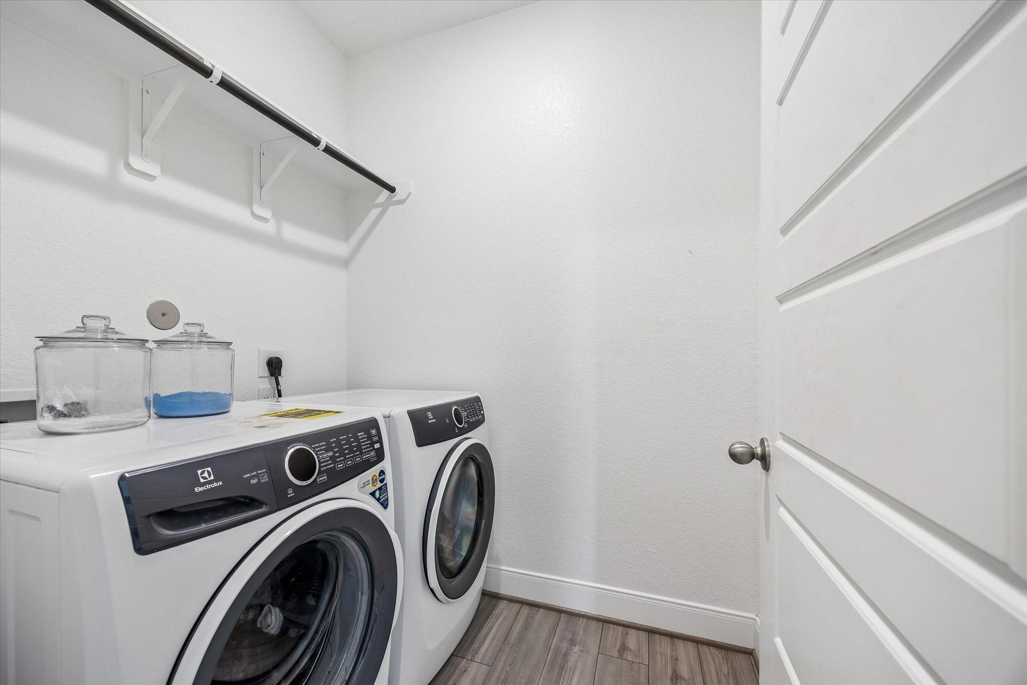 Laundry room with front-loading washer and dryer, overhead hanging rod, and glass storage jars.