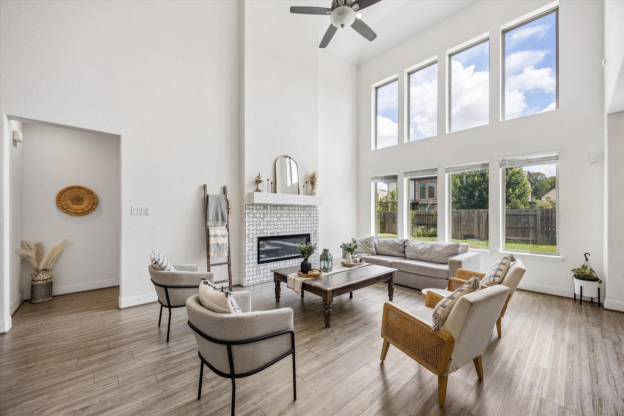 Staged living room with a tiled fireplace, vaulted ceiling, and tall windows overlooking the backyard.