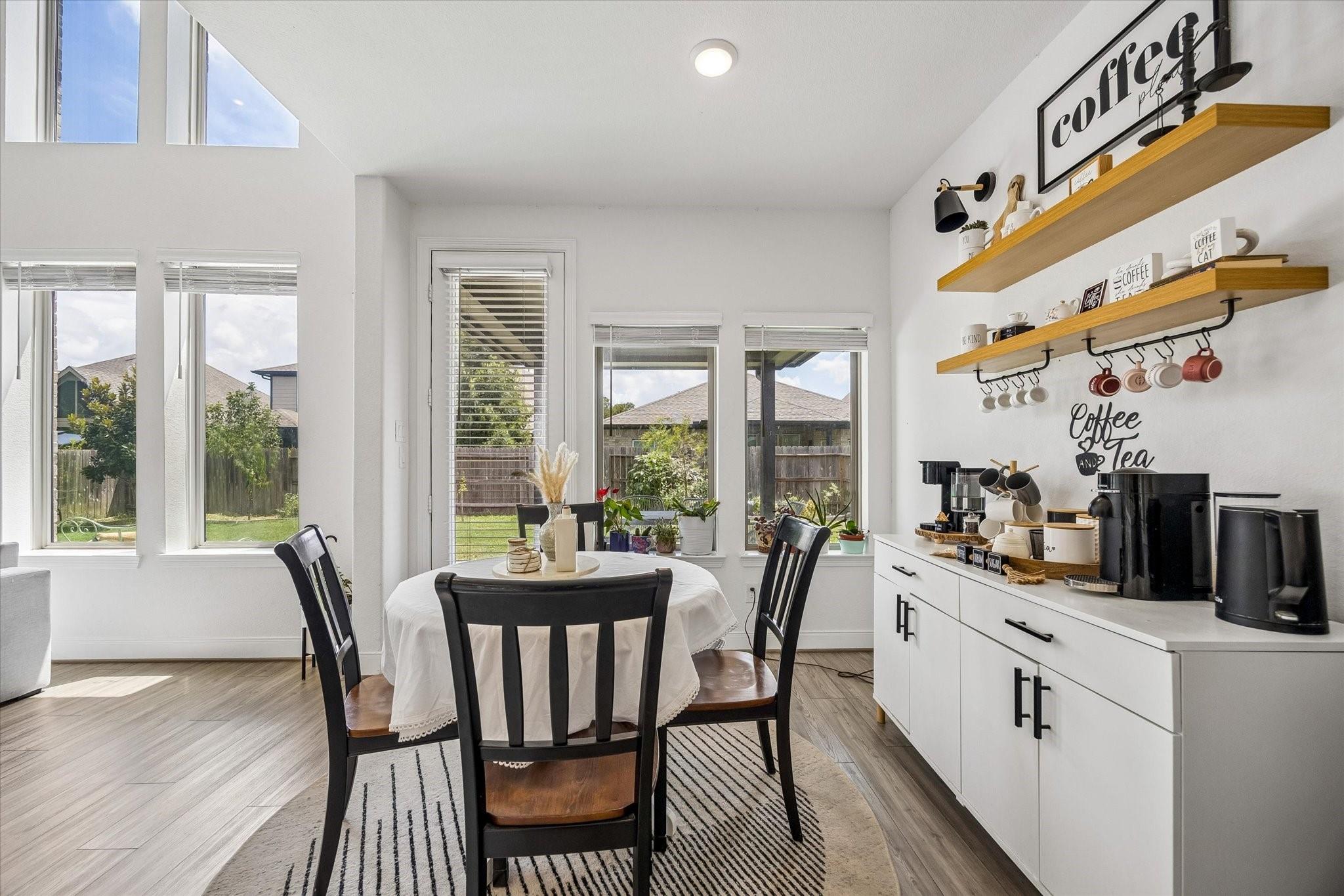 Dining area with a round table beside a built-in coffee bar and floating wood shelves.