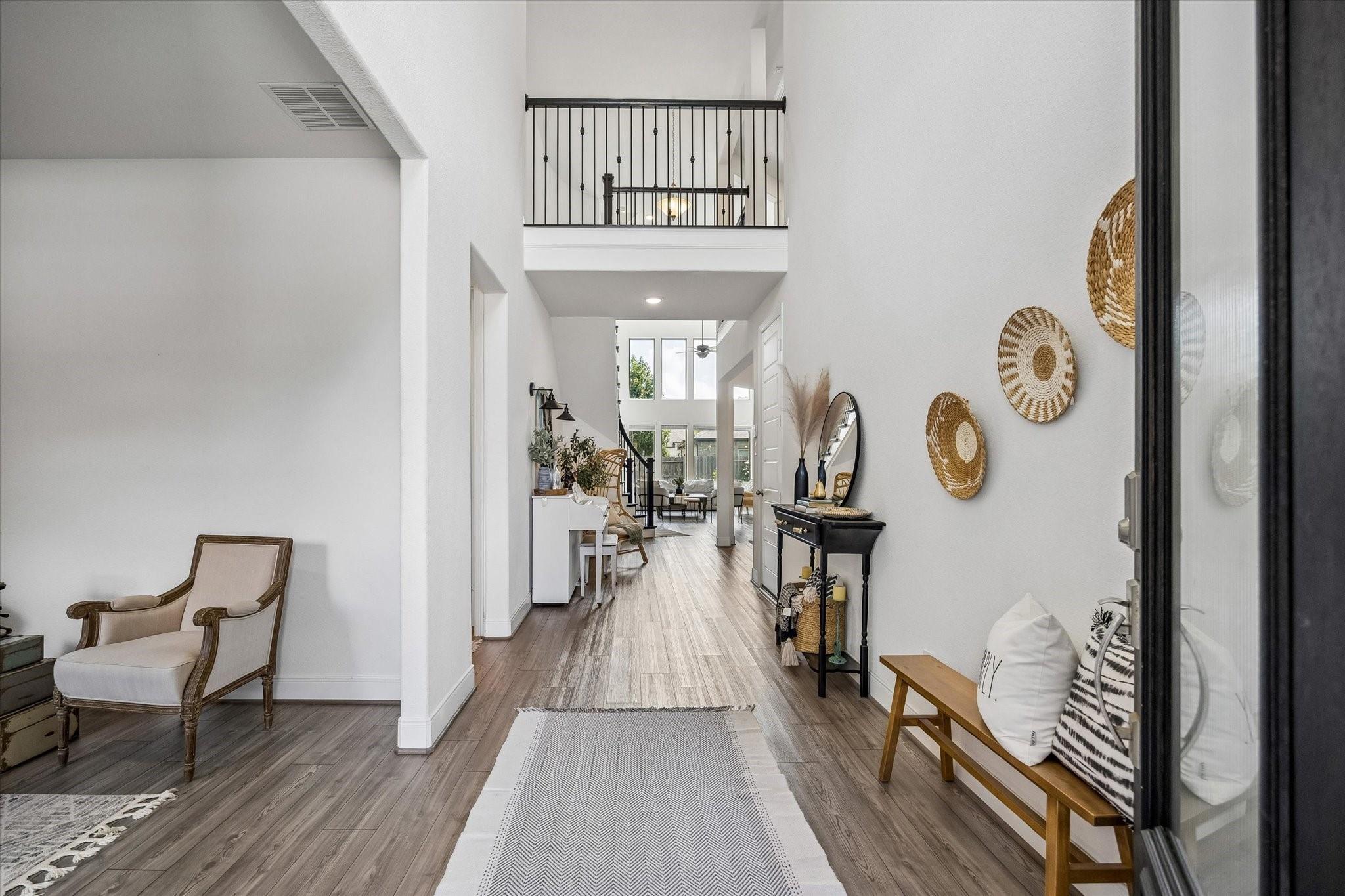 Furnished two-story entry hall with wood-look floors, a long runner, and a black-railed upstairs landing.