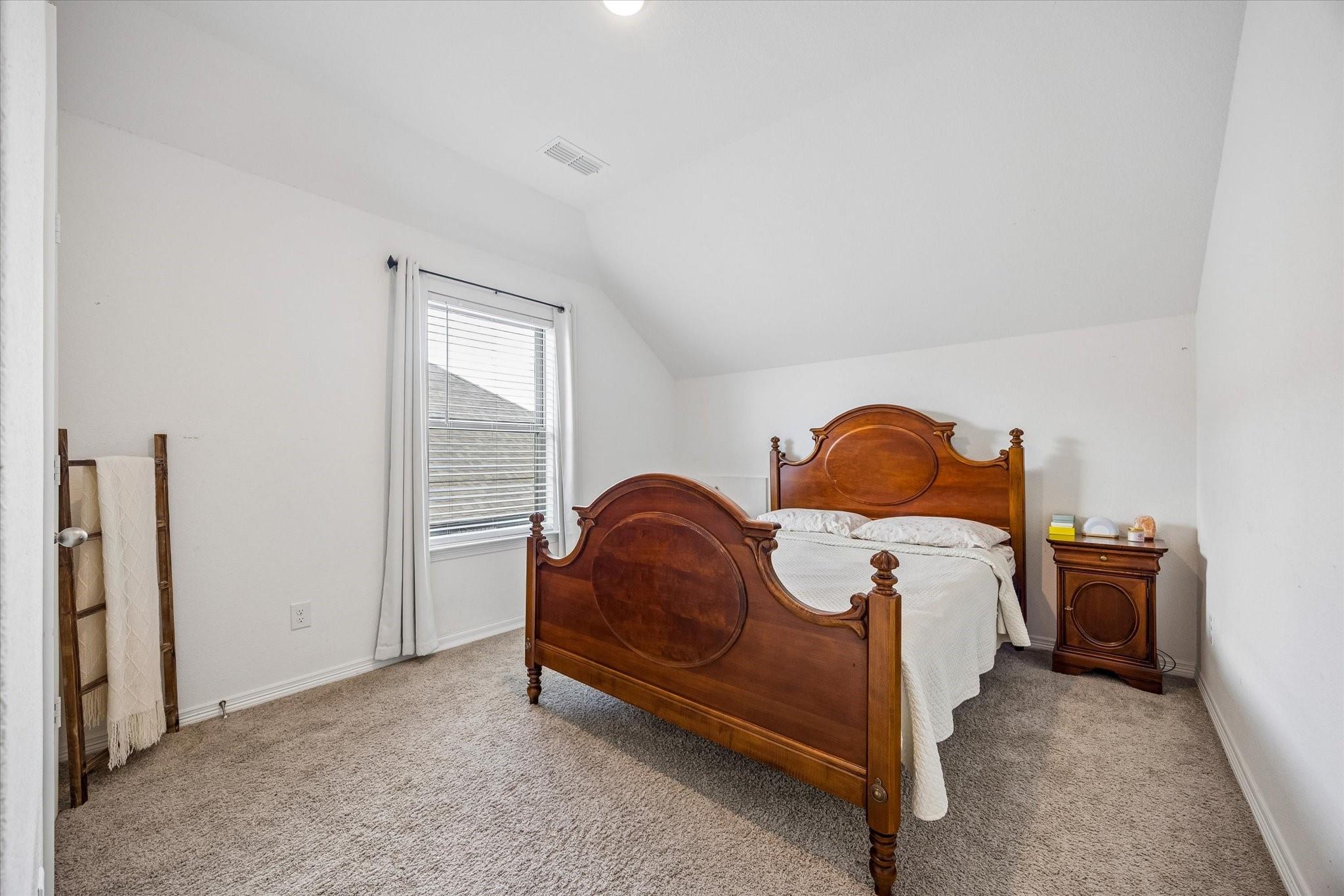Furnished bedroom with a traditional wooden bed, vaulted ceiling, and beige carpet.
