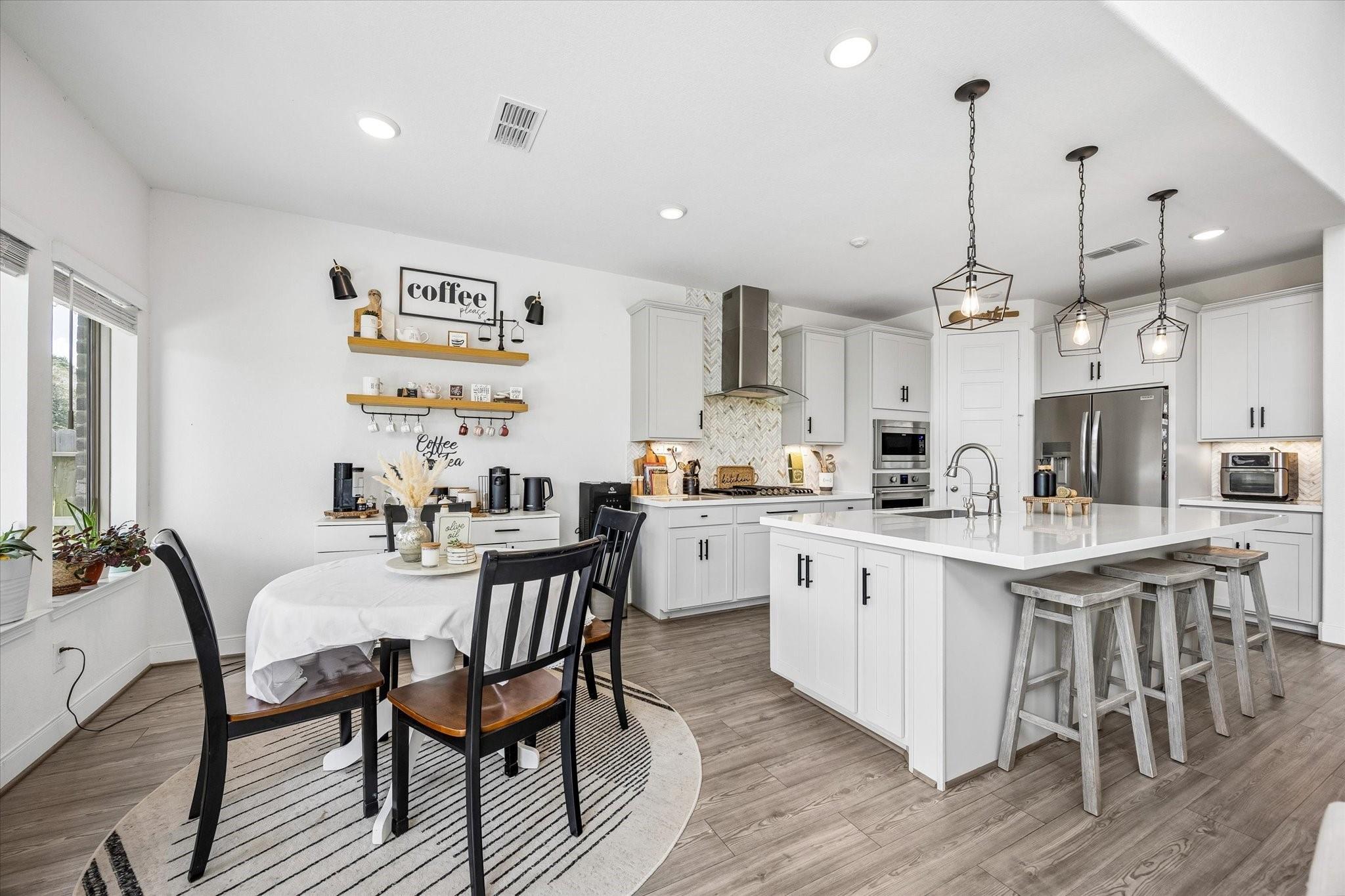 Bright white kitchen with a large island, gray stools, and an adjoining round dining table.