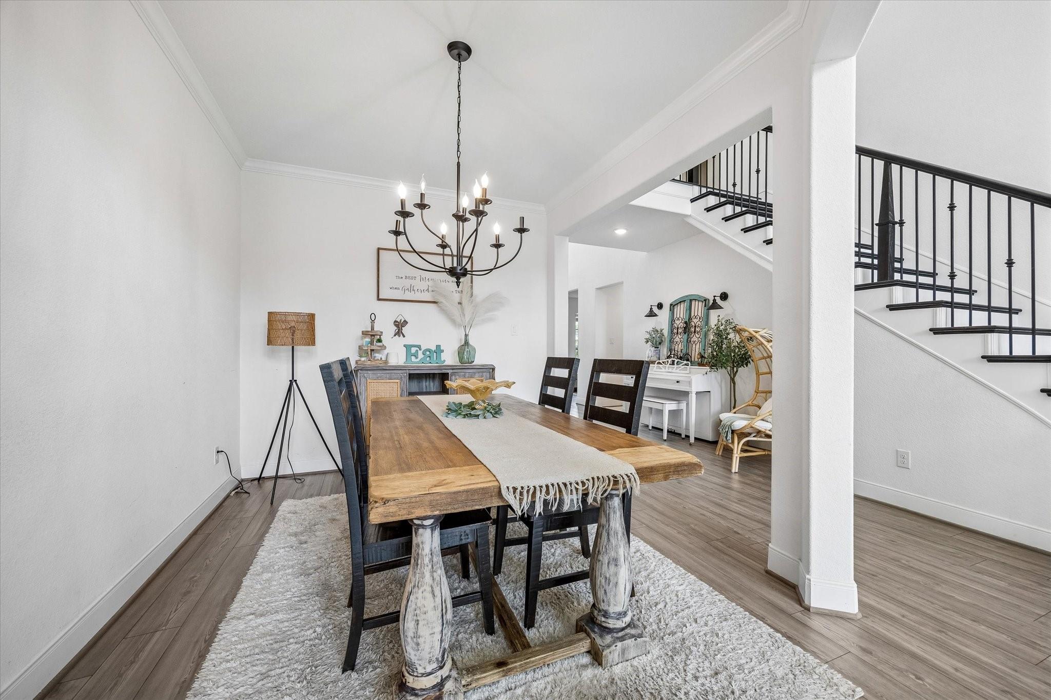 Dining room with a rustic wood table, dark chairs, and a black chandelier beside an open staircase.