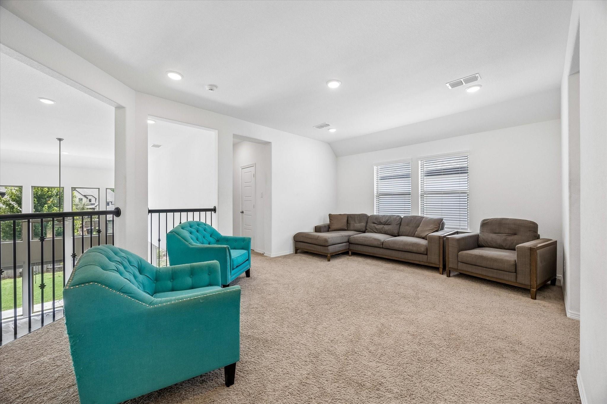 Upstairs living room with teal armchairs, brown seating, beige carpet, and a black overlook railing.