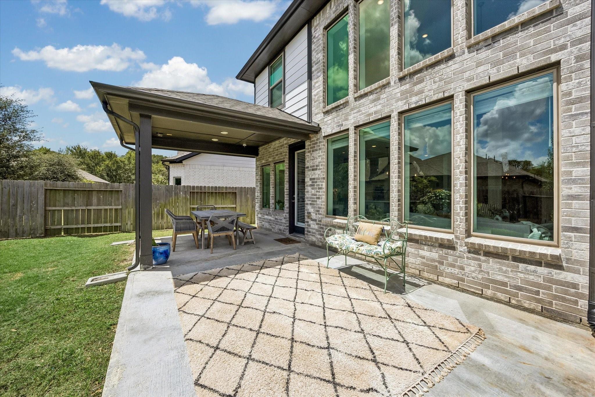 Backyard patio with covered dining area, brick exterior, outdoor bench, and patterned rug.