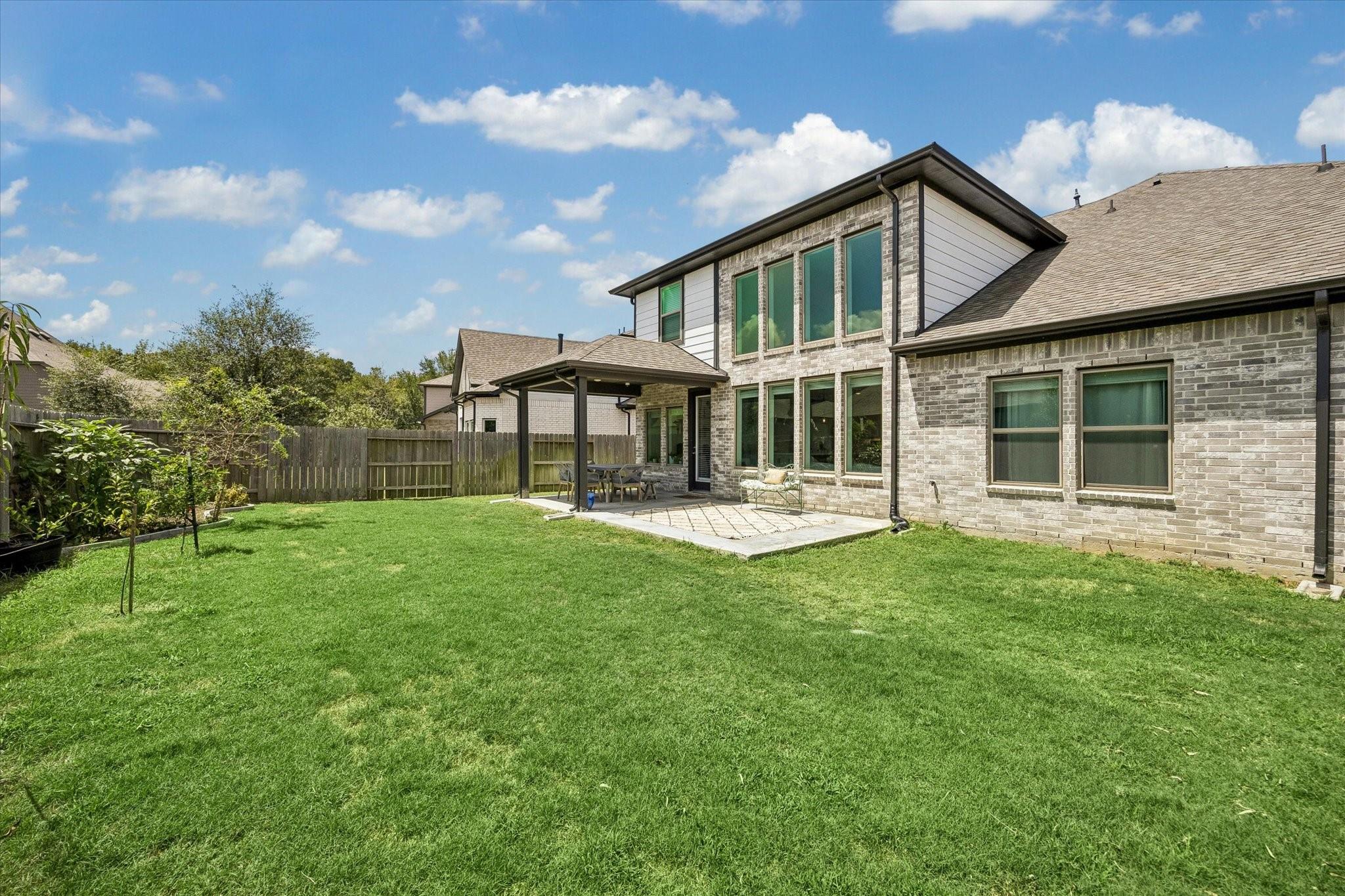 Two-story brick house behind a broad lawn, with a fenced yard and covered patio.