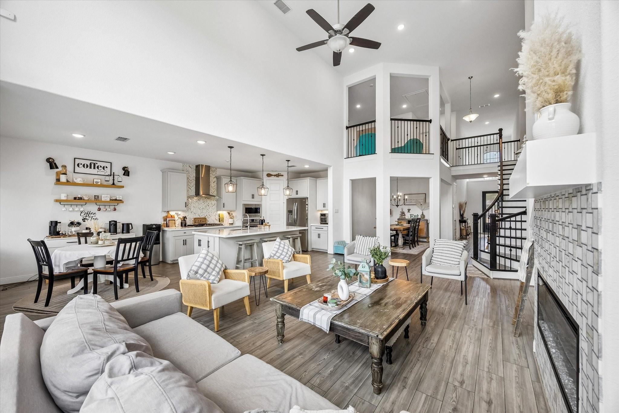 Open-concept living room, dining area, and kitchen with a two-story ceiling and dark-railed staircase.