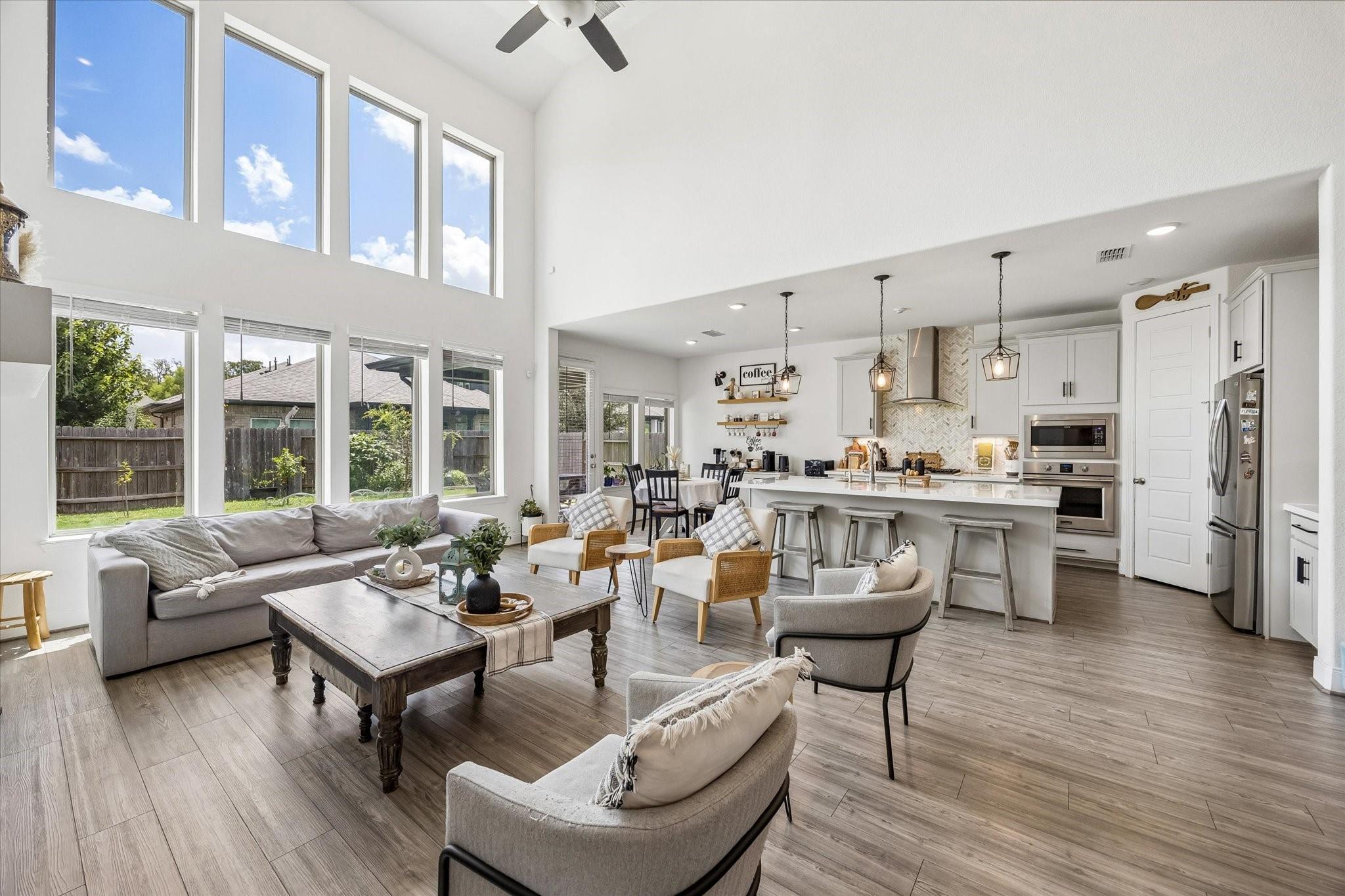 Open-plan living room and kitchen with double-height windows, a gray sofa, and a white island.